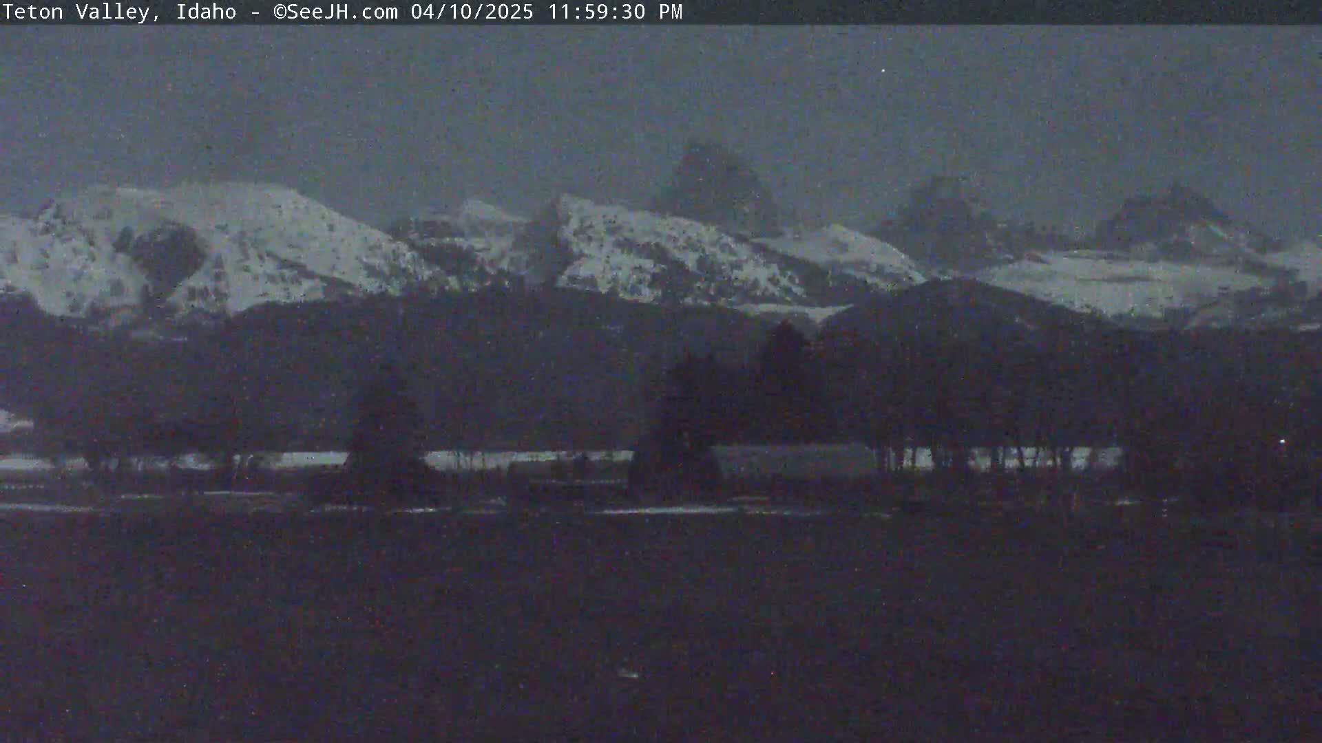 Snow-capped mountains are visible at dusk, behind a dark foreground of trees and flat land.