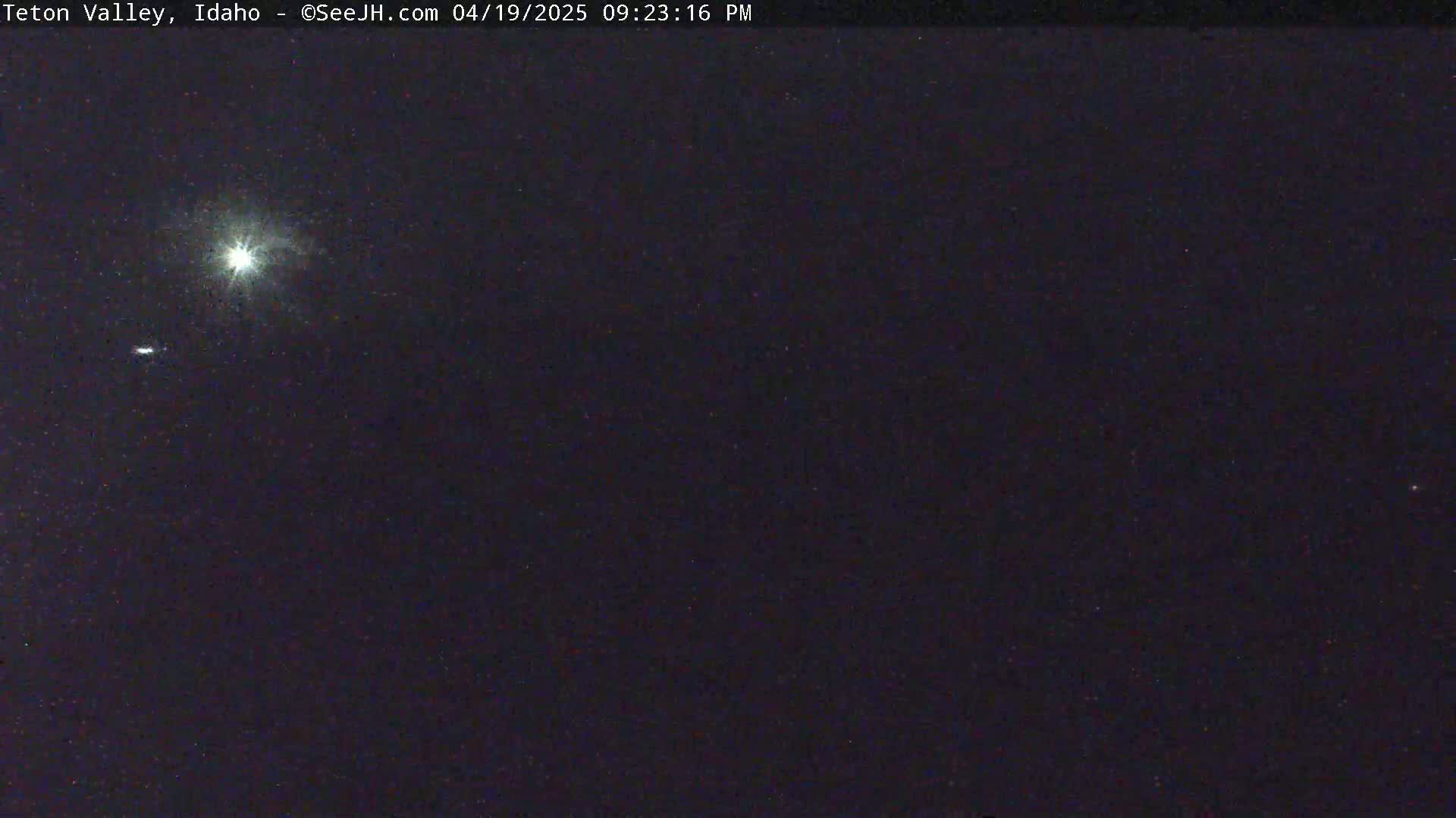 A bright light source, possibly the moon, is visible in a dark night sky with a few faint stars.
