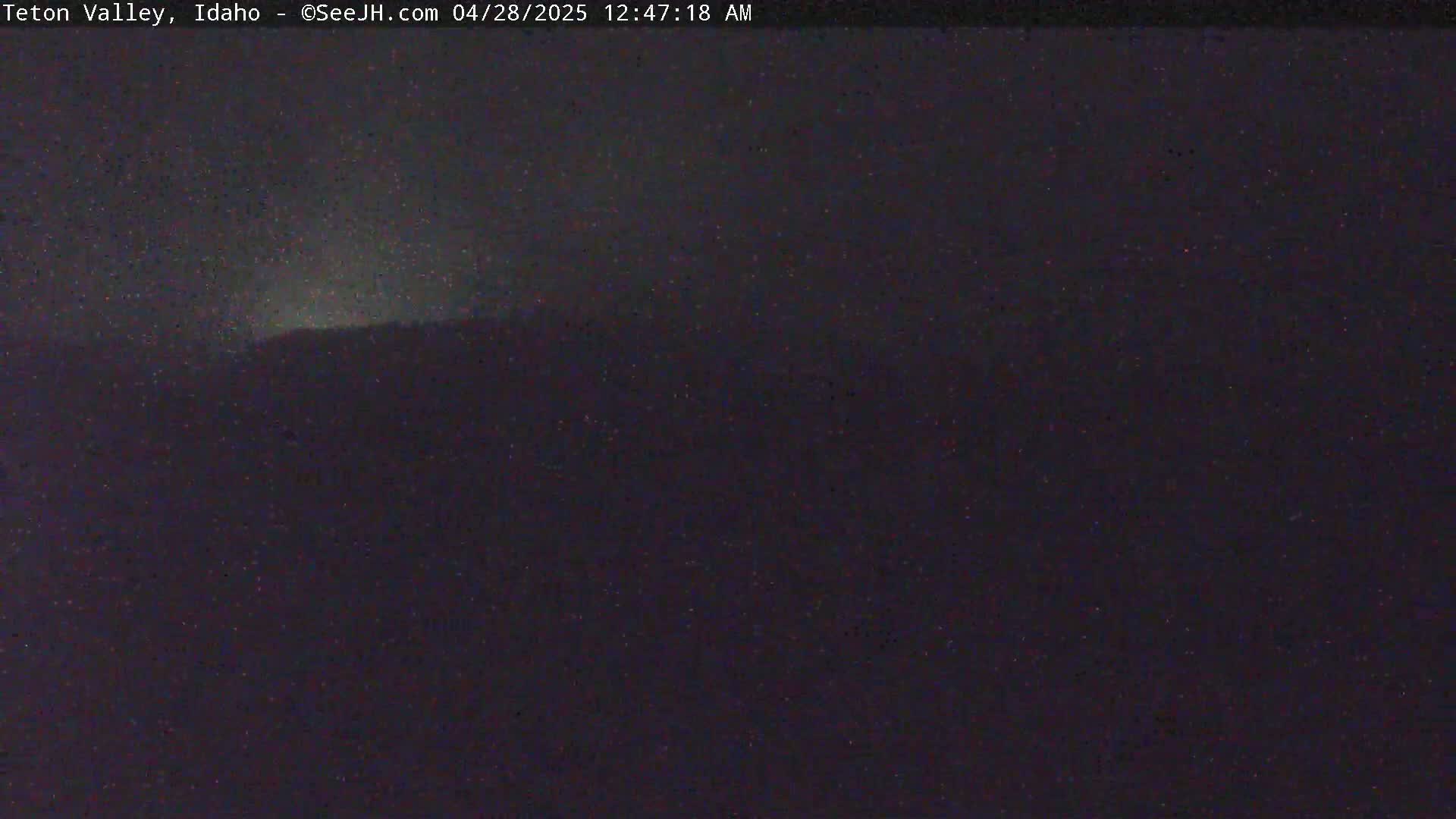 A dark, nighttime view shows a dimly lit mountain range under a mostly clear sky.