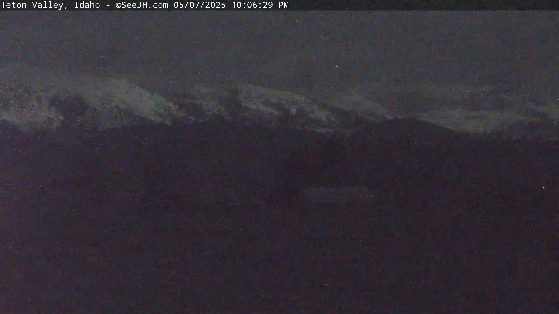 A dark, nighttime view shows snow-capped mountains under a mostly clear, dusky sky.