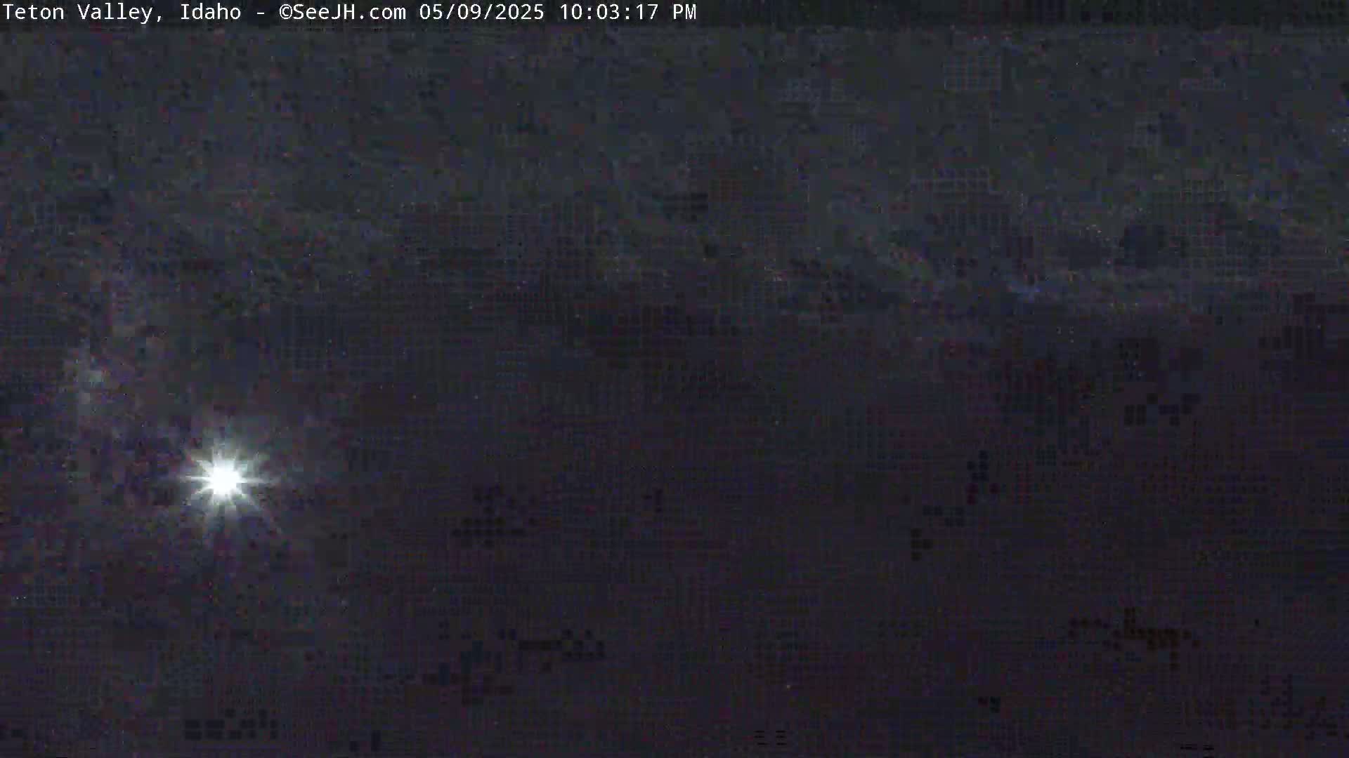 A bright, star-like light shines in a dark night sky with faint clouds or atmospheric haze.