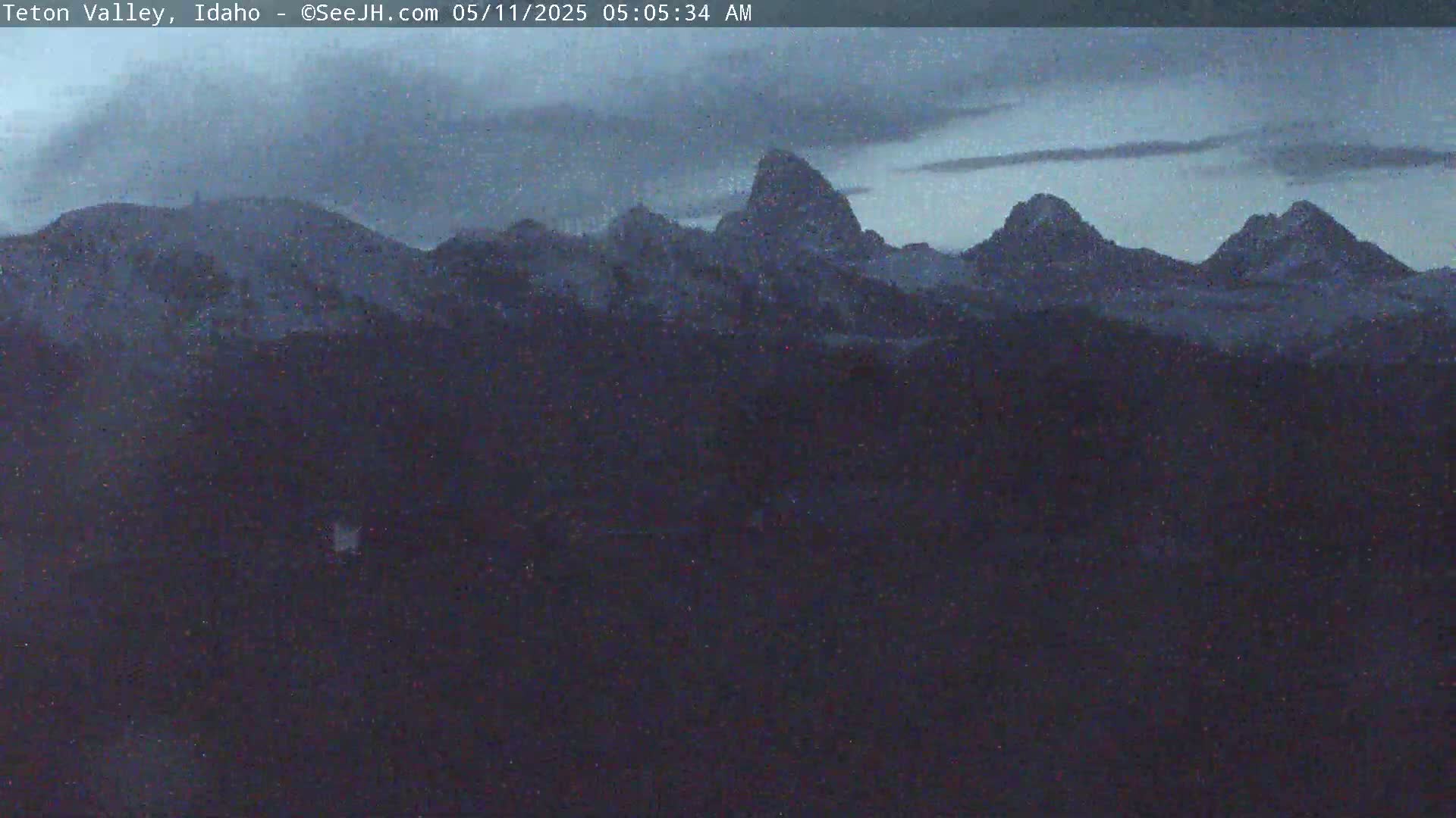Snow-covered mountains are visible under a dark, cloudy sky at dawn.