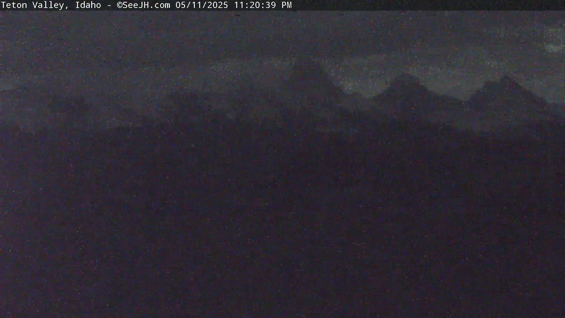 A nighttime, long shot of dark mountains under a cloudy sky.