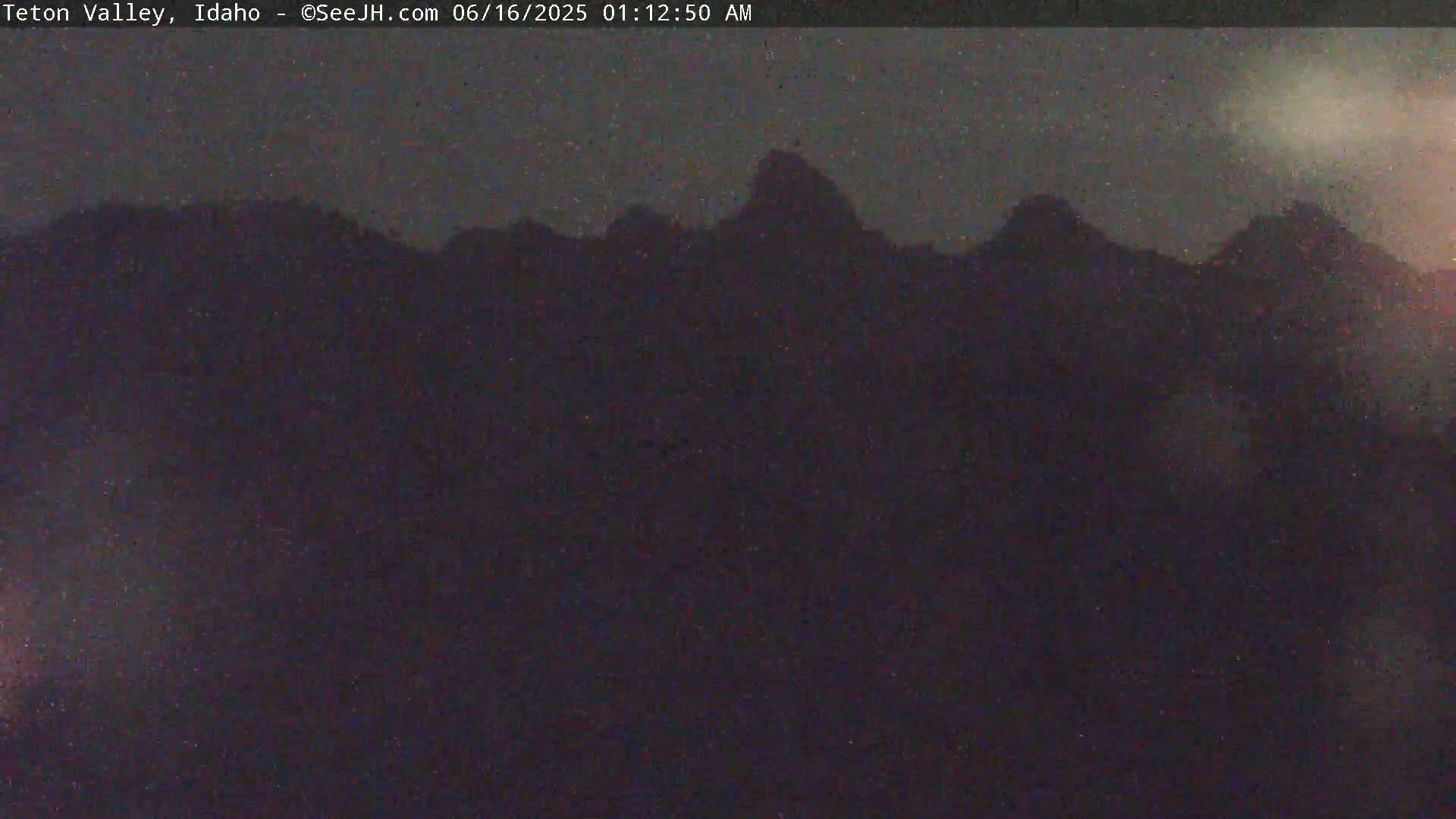A dark, nighttime image shows a silhouetted mountain range under a mostly clear sky.