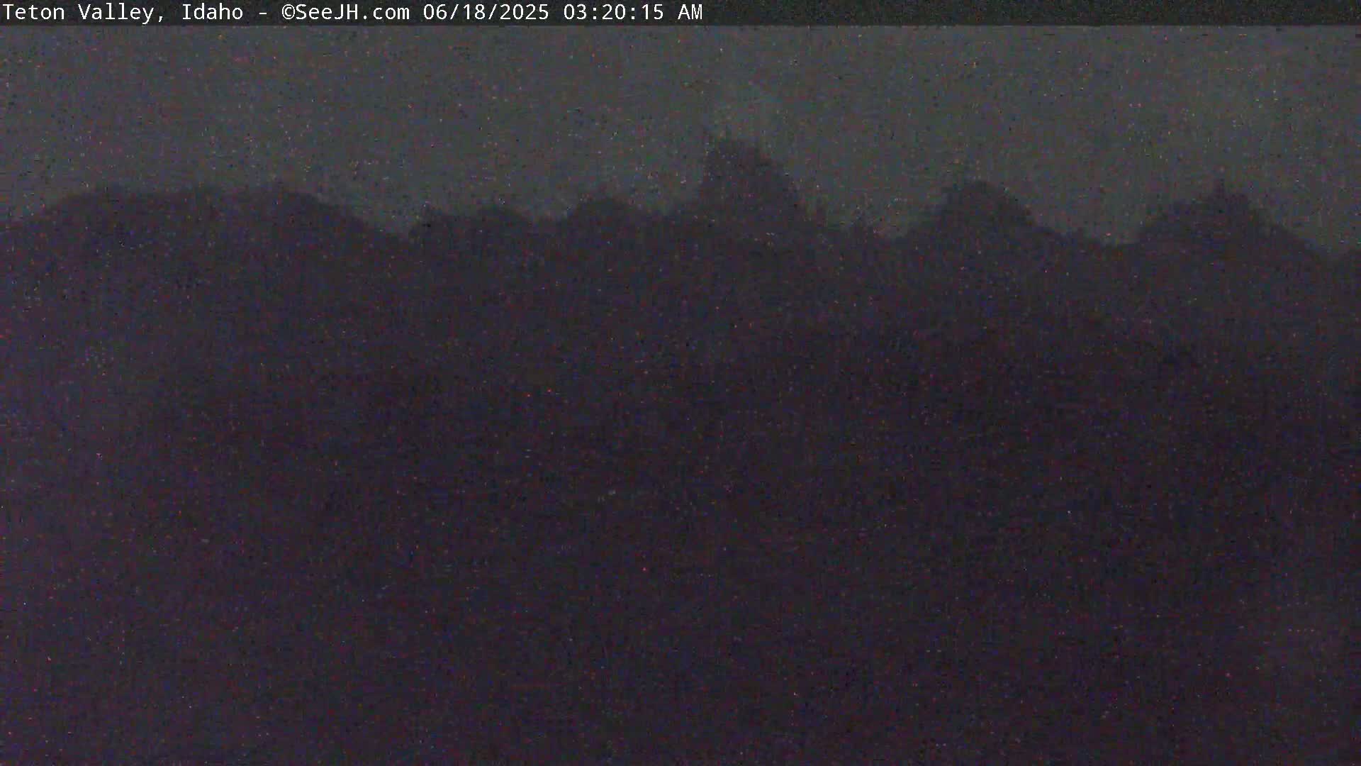 A dark, nighttime image shows a silhouetted line of trees and hills under a mostly clear, dark sky.