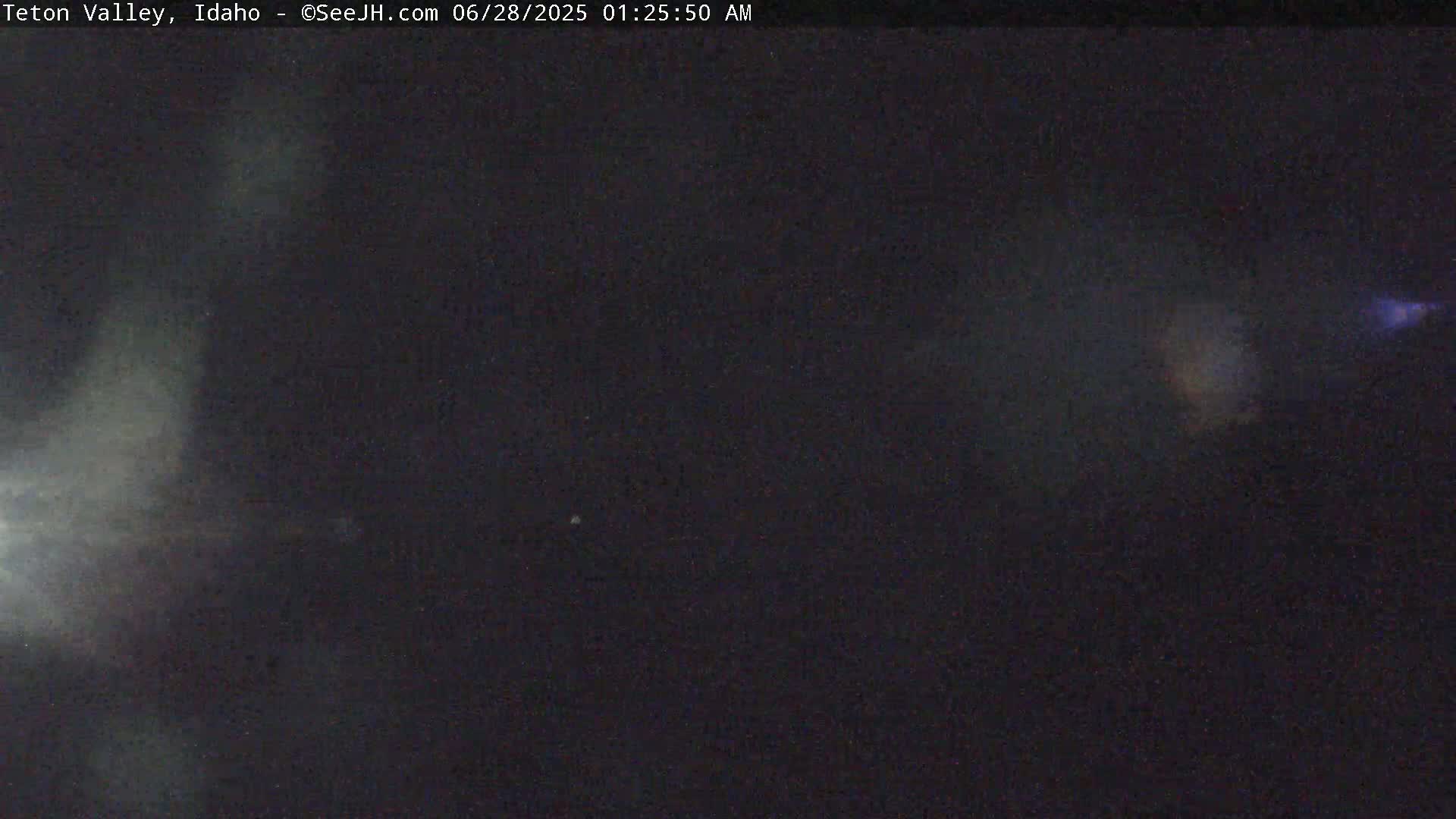 A dark, nighttime scene shows a hazy, indistinct view with faint light sources.