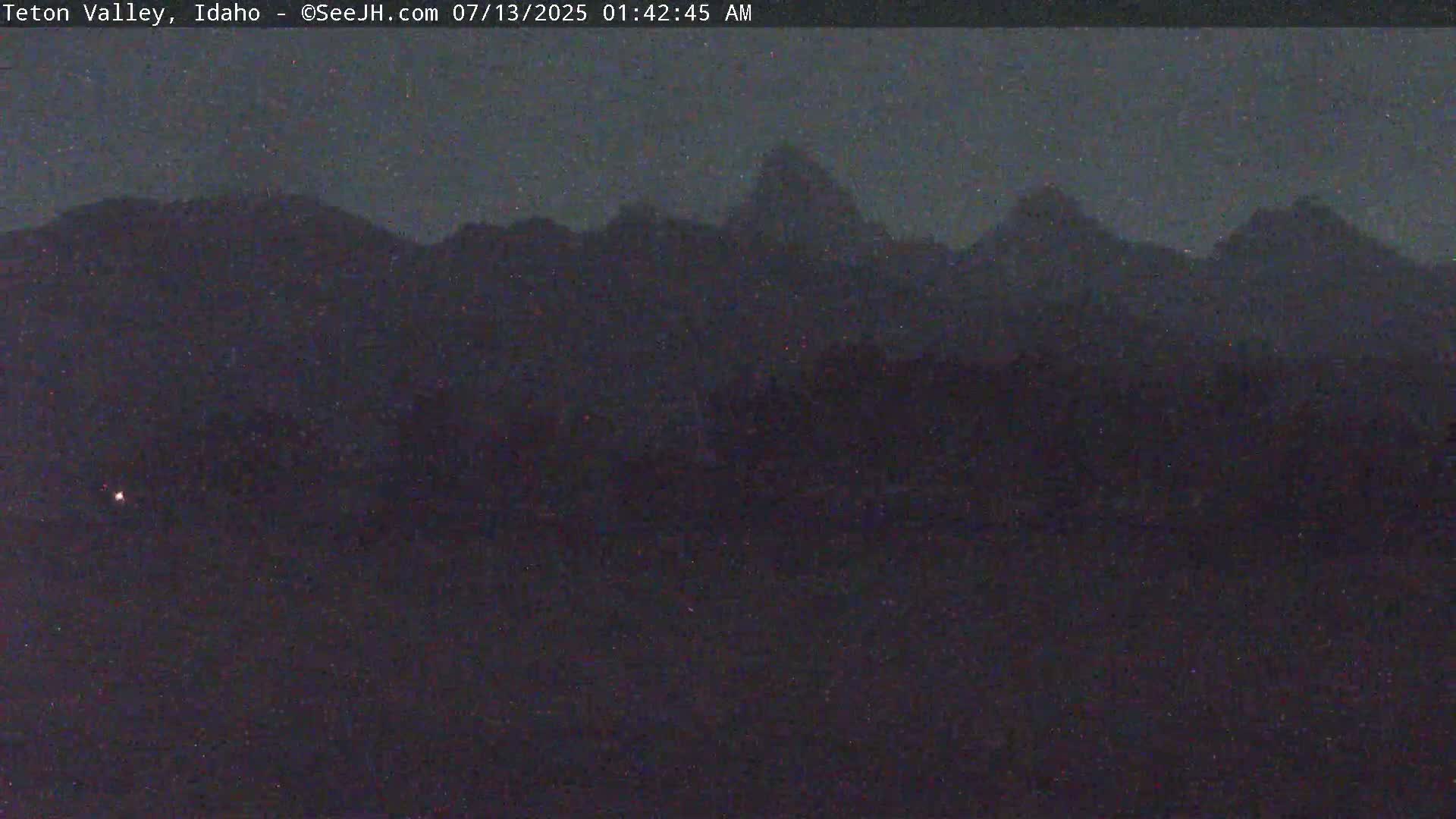 A dark, nighttime image shows a mountain range silhouetted against a slightly lighter sky.