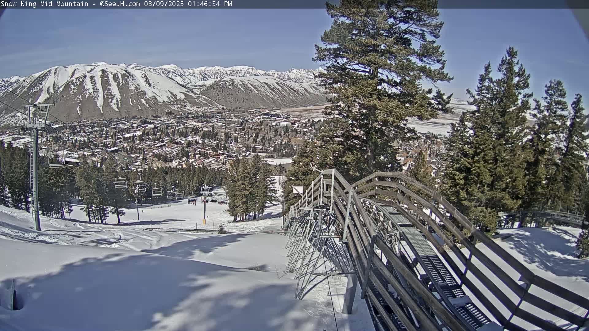 A snow-covered mountain slope with a ski lift and a town in the background on a sunny day.