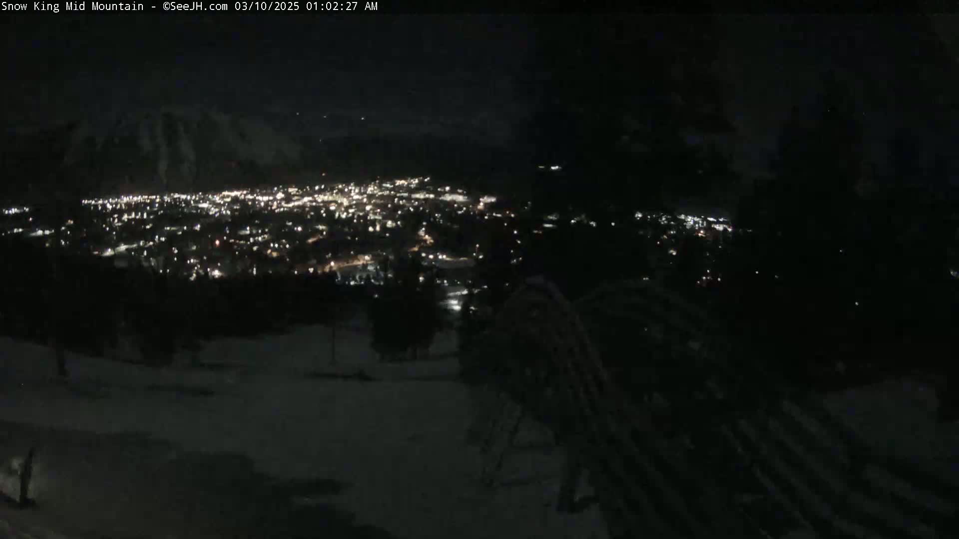 A nighttime view from a snowy mountain overlooking a city illuminated by many lights.