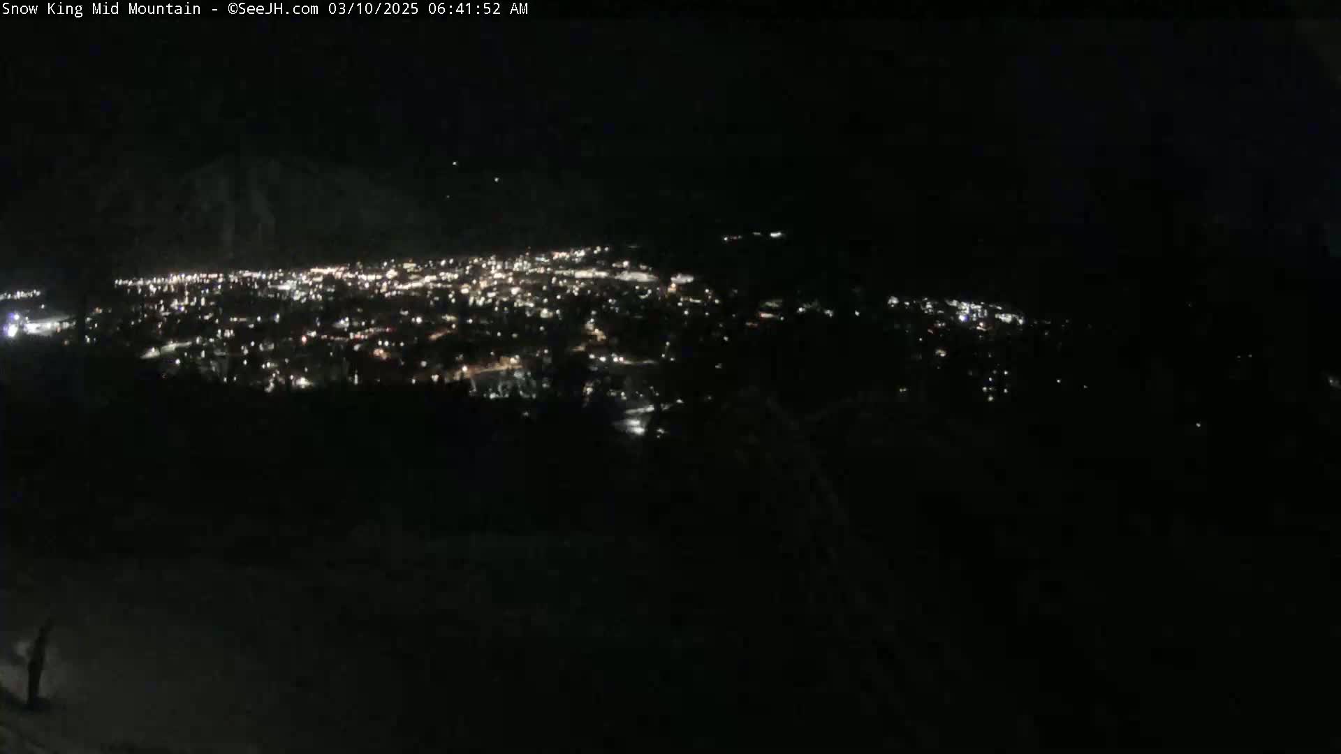 A nighttime, long-range view of a city's lights spread across a valley, seen from a high vantage point.