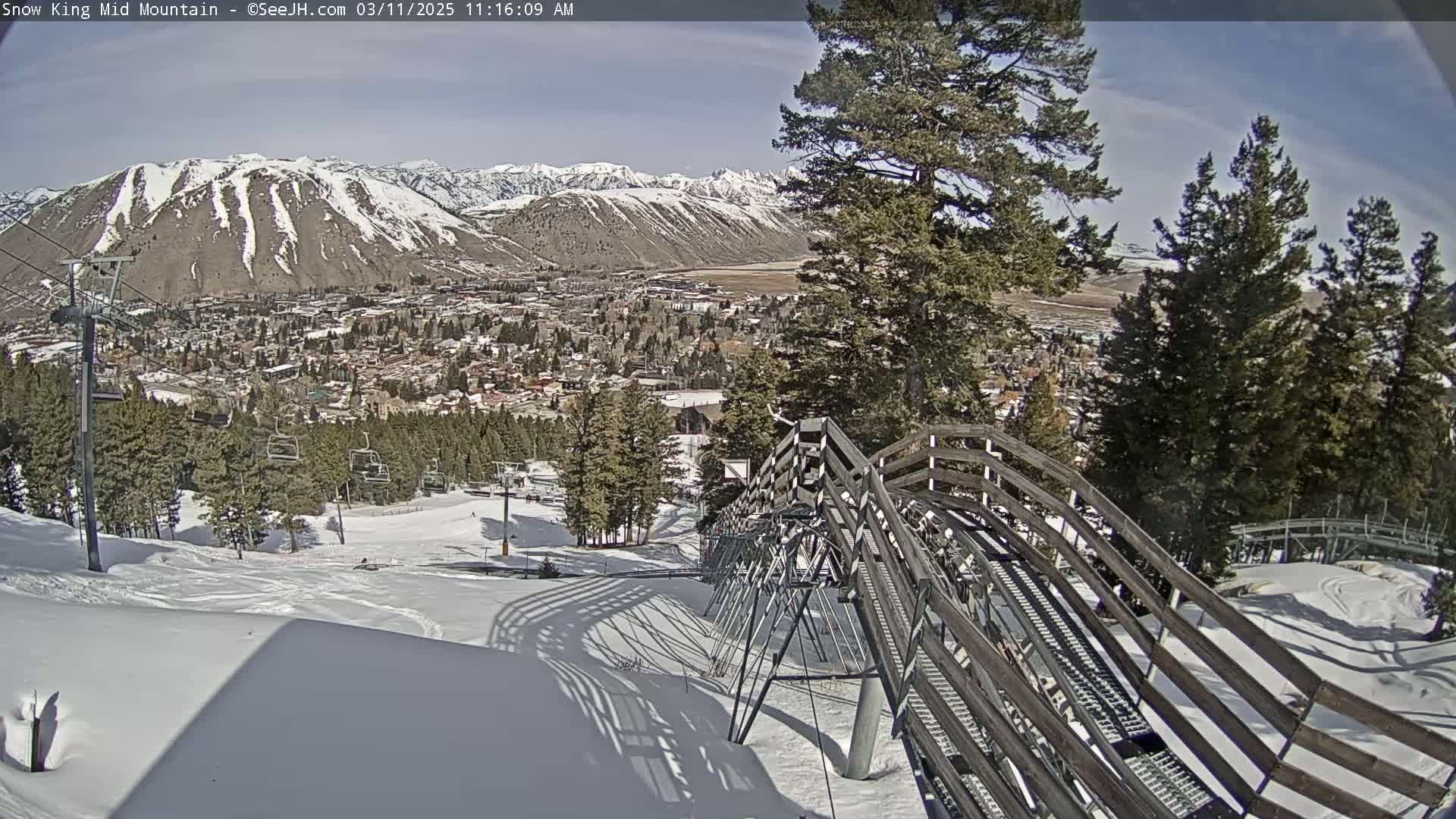 A snow-covered mountain slope with a ski lift and town in the background under a sunny sky.