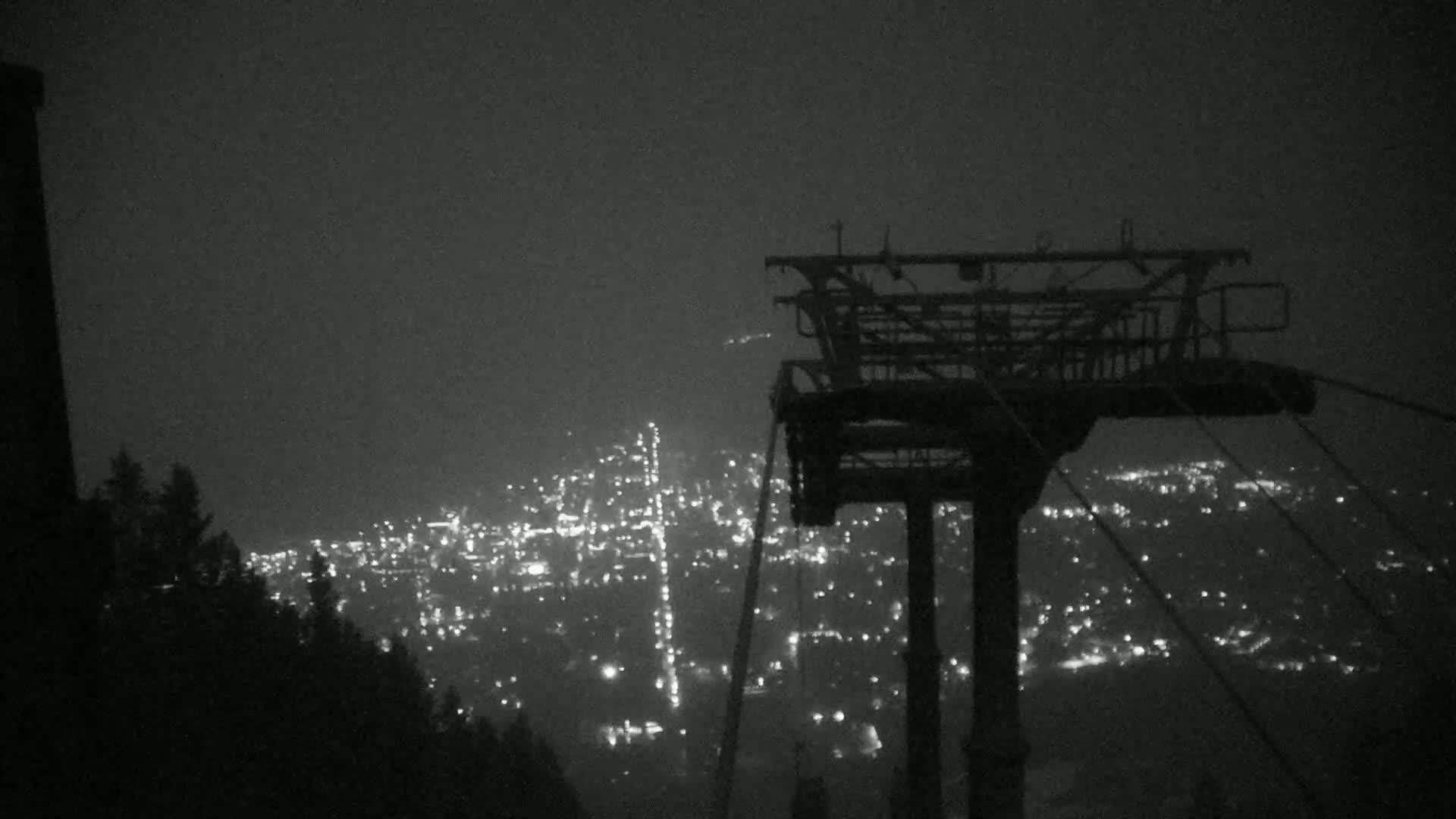 A nighttime view from a chairlift shows a hazy city glowing with lights below.