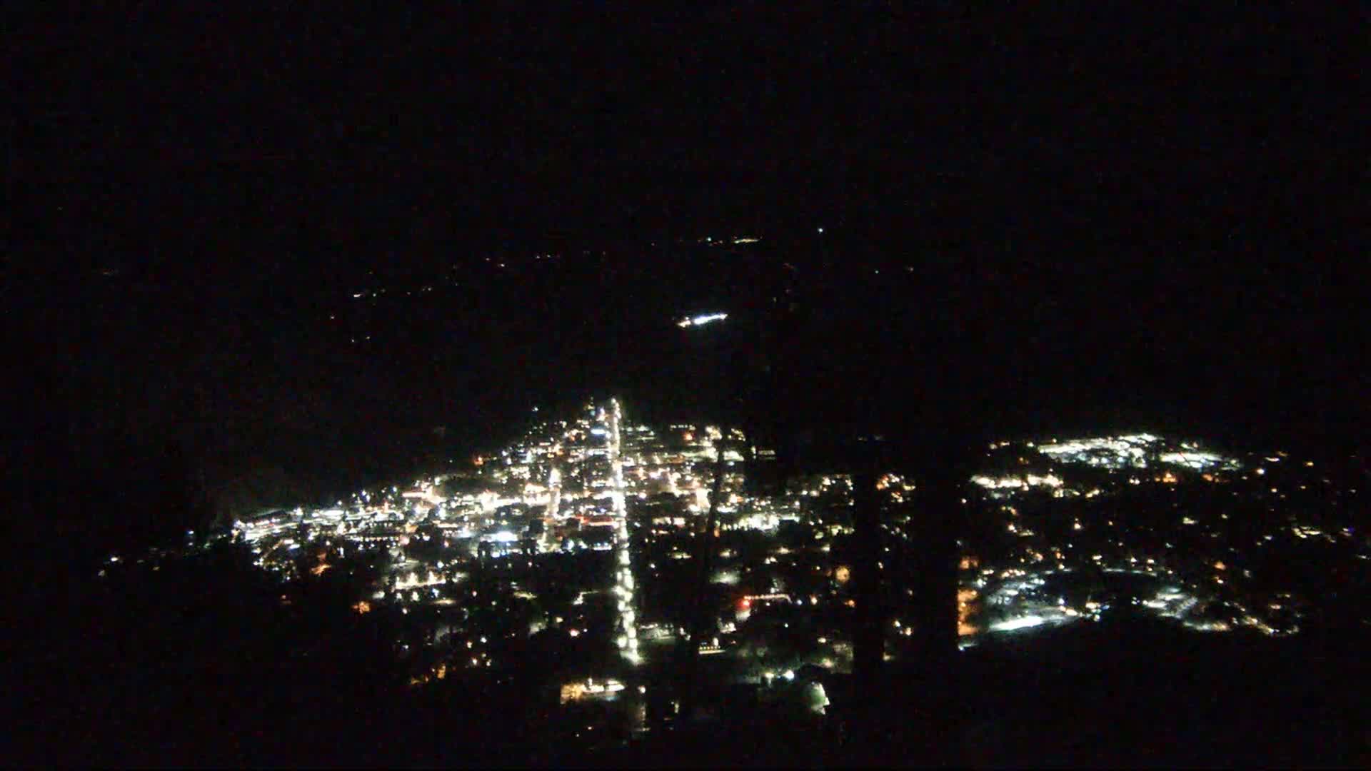 A nighttime aerial view shows a town's illuminated streets and buildings spread across a dark landscape.