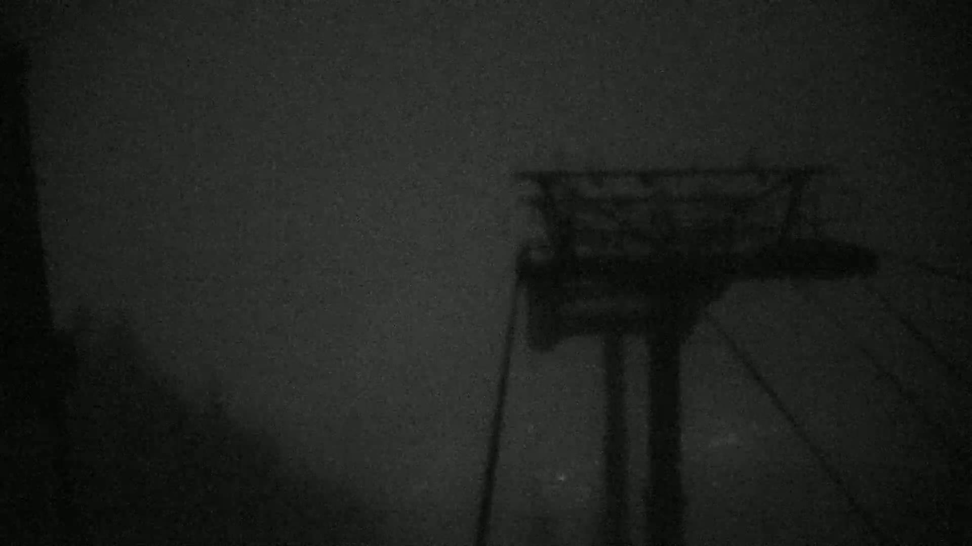 A dark, shadowy image shows a ski lift structure under foggy or snowy conditions at night.