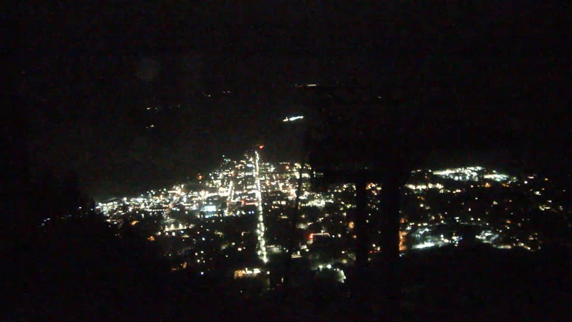 A nighttime, aerial view shows a city illuminated by many small lights, spread out across a valley.