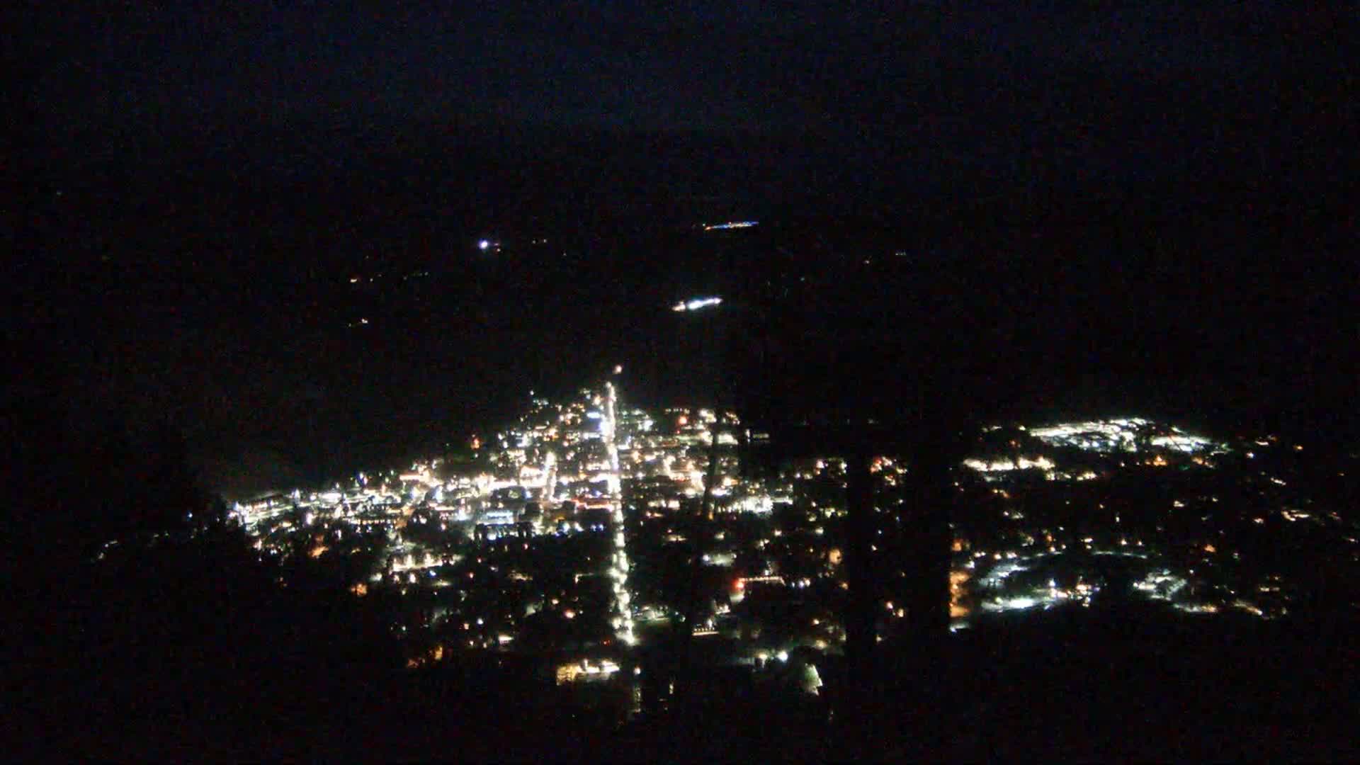 A nighttime, high-angle view shows a small town illuminated by numerous lights, extending across a dark landscape.