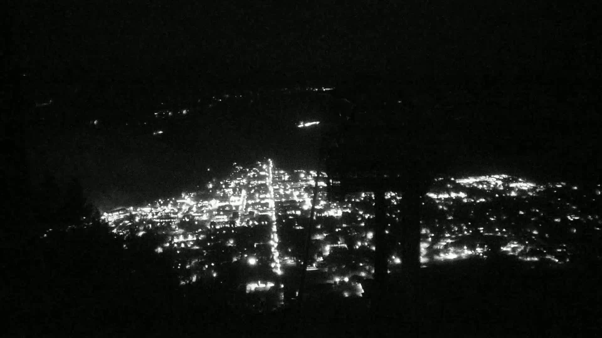 A nighttime, high-angle view shows a city illuminated by numerous lights spread across a dark landscape.