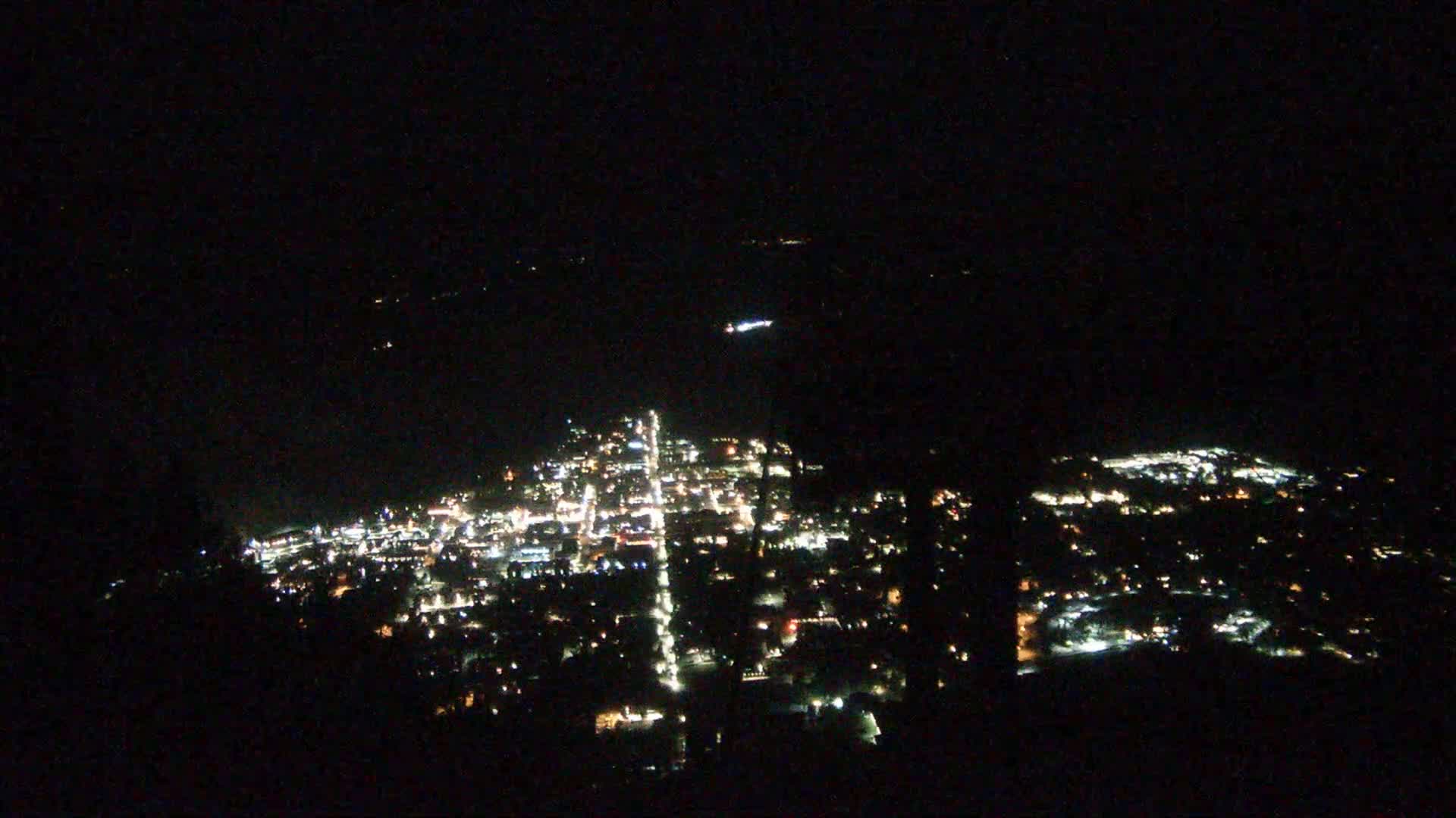 A nighttime, high-angle view shows a city's illuminated streets and buildings spread across a dark landscape.