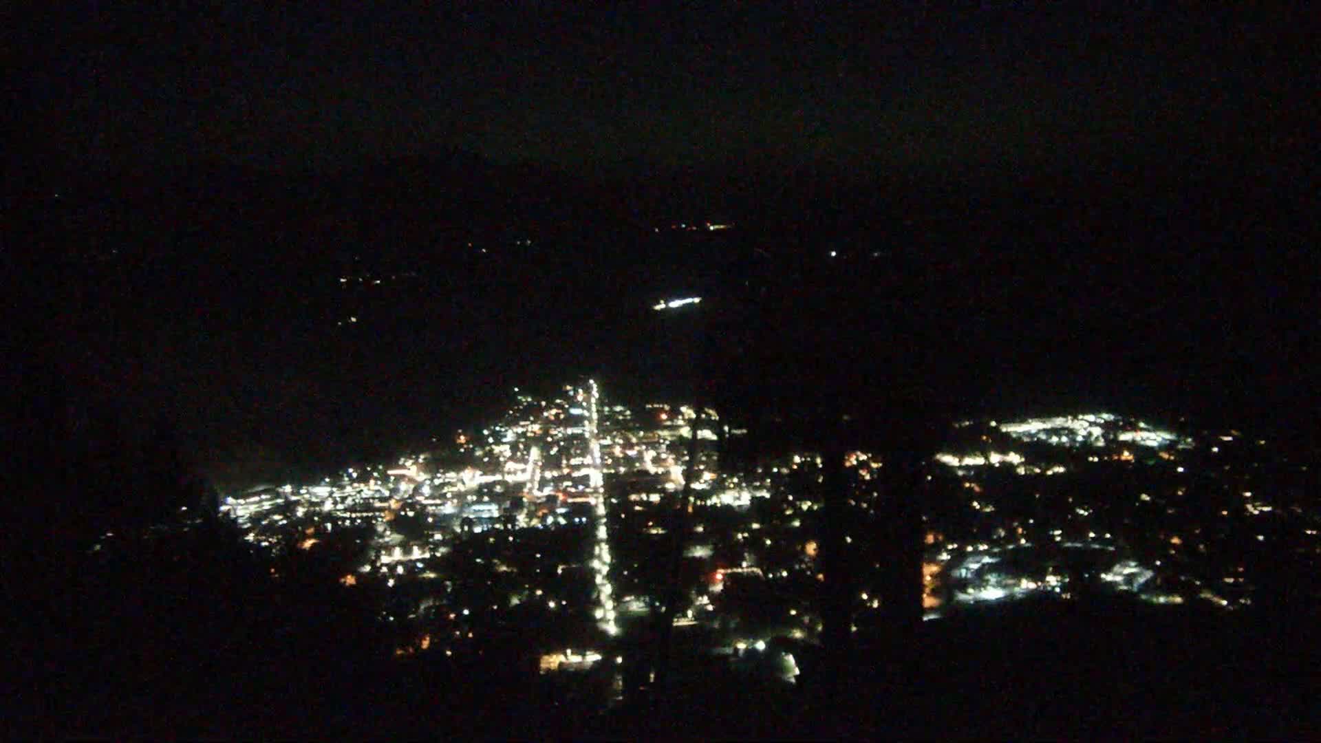 A nighttime, high-angle view shows a city's lights spread across a valley.