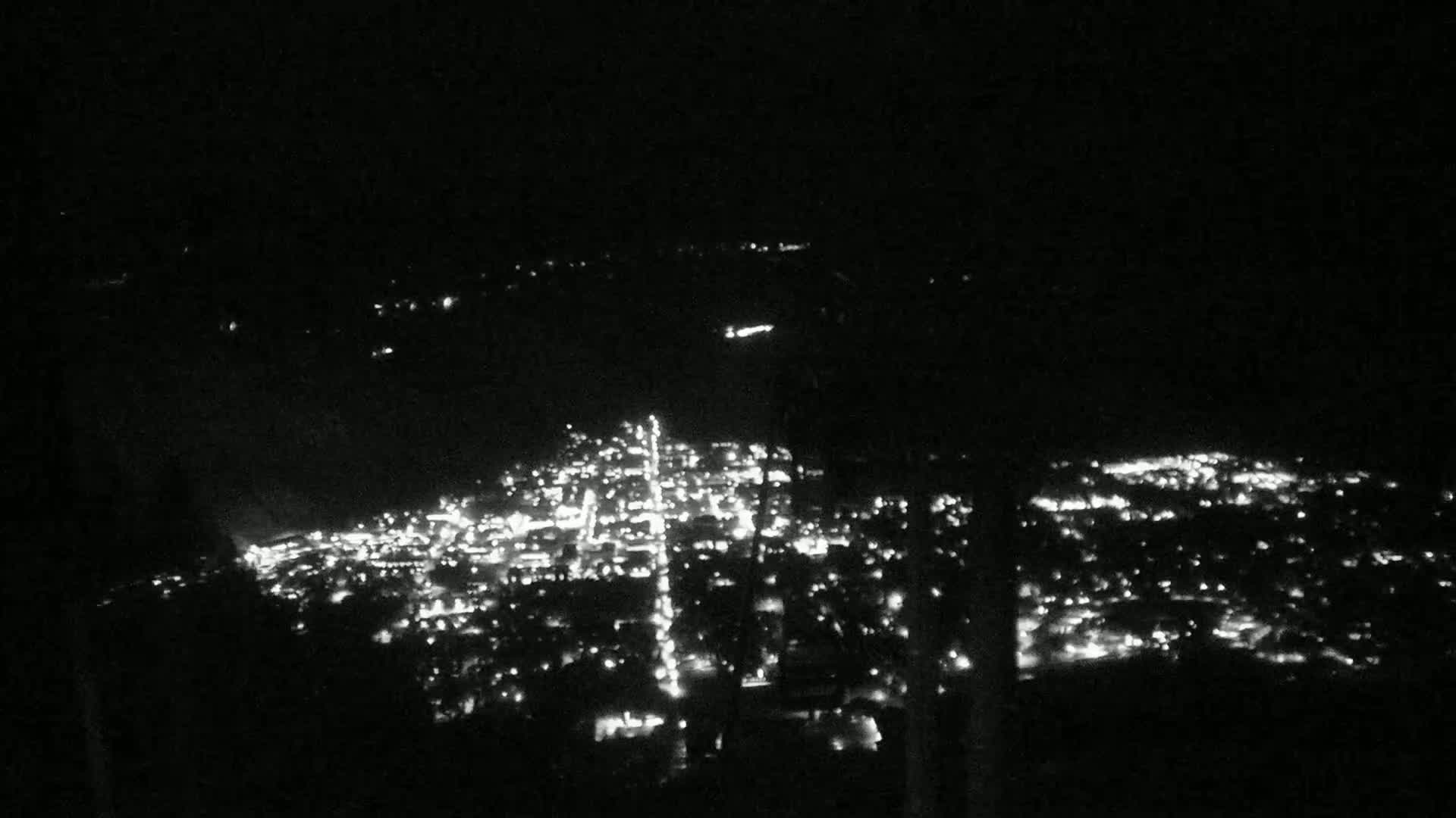 A nighttime aerial view shows a city illuminated by numerous lights spread across a dark landscape.