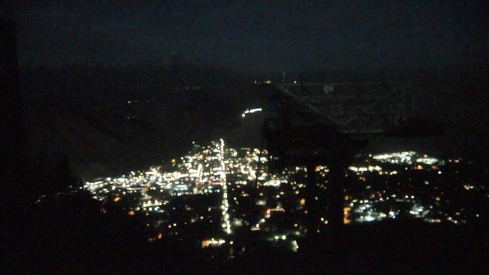 A nighttime, aerial view shows a city's lights spread across a valley, under a dark sky.