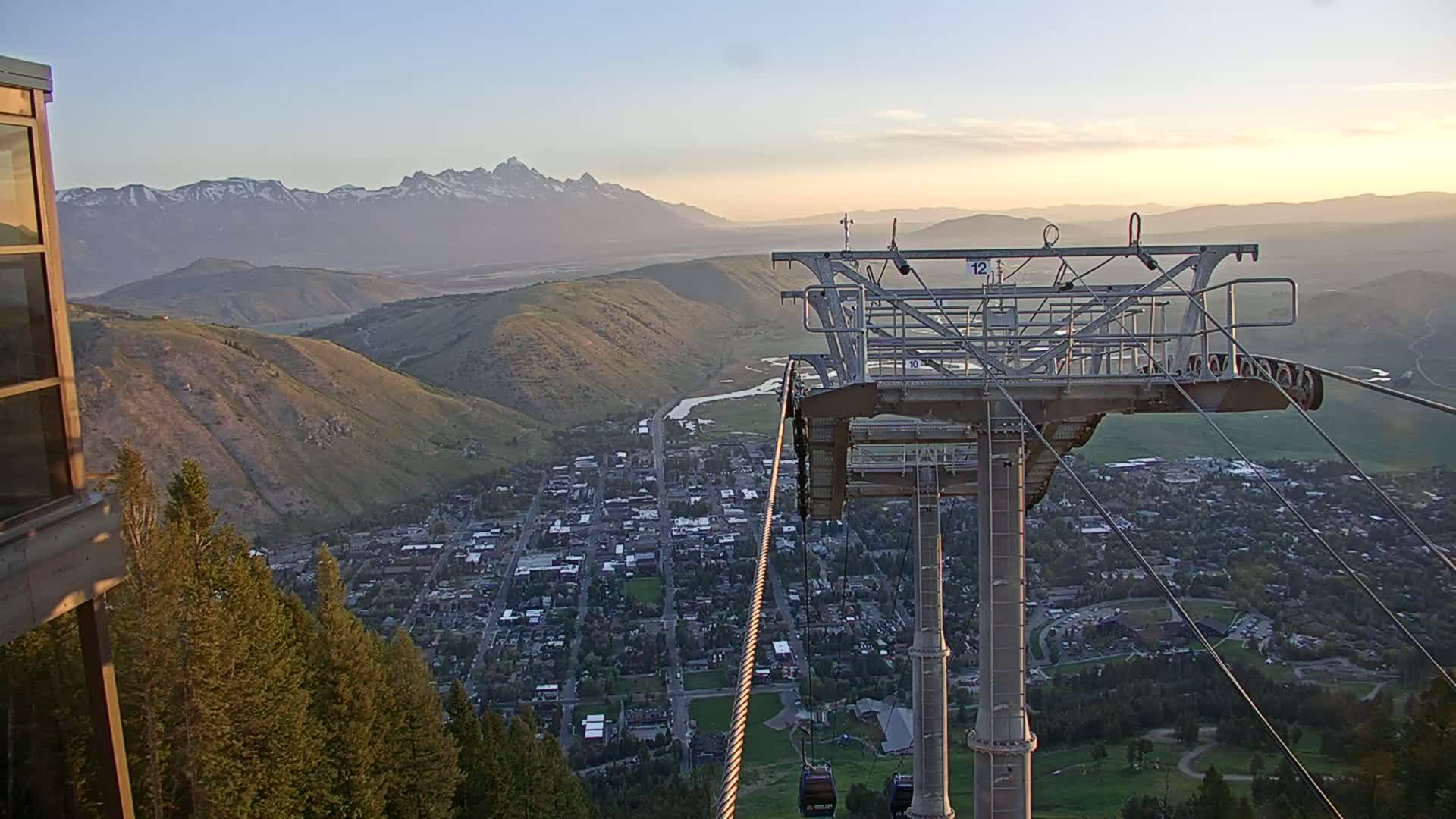 A chairlift overlooking a valley town at sunset, with snow-capped mountains in the distance.