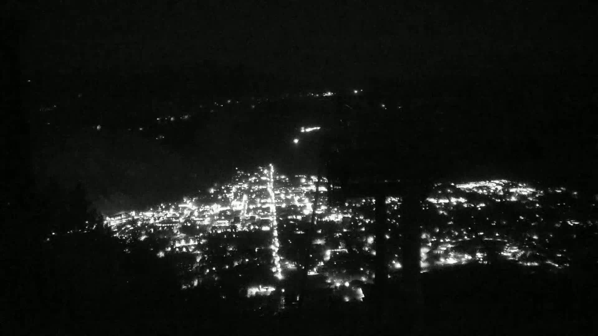 A nighttime, aerial view shows a city illuminated by numerous lights spread across a dark landscape.