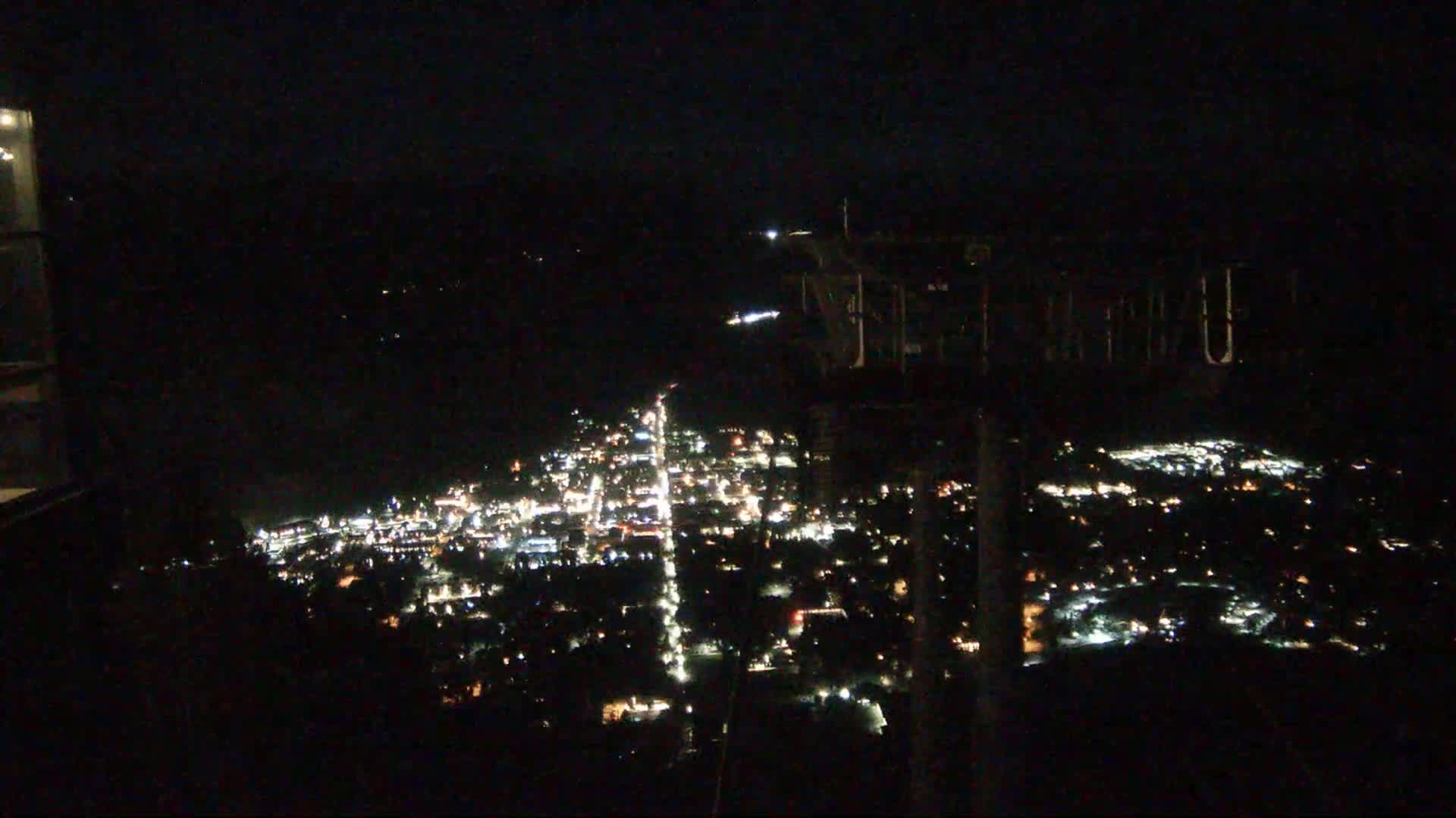 A nighttime, high-angle view shows a town's lights spread across a valley.