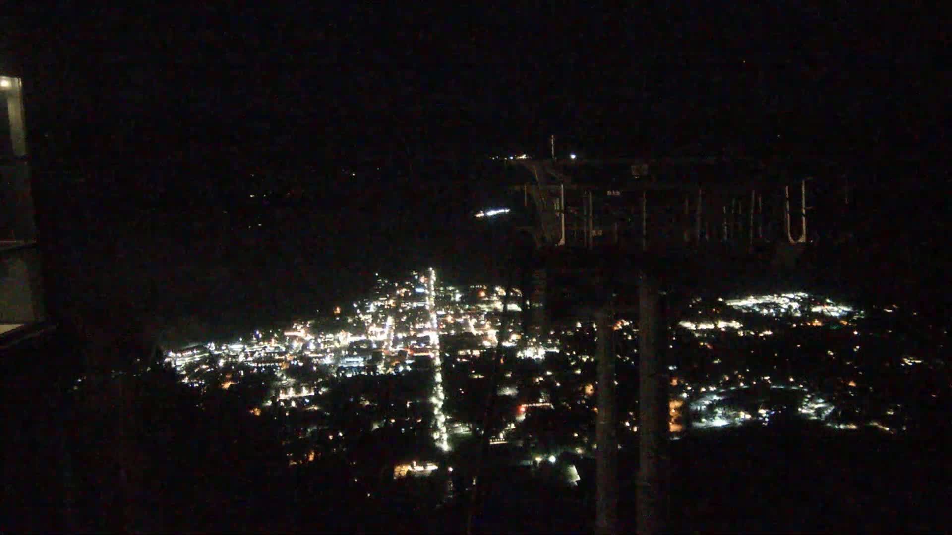 A nighttime, high-angle view of a city illuminated by many small lights, extending to a dark body of water in the distance.