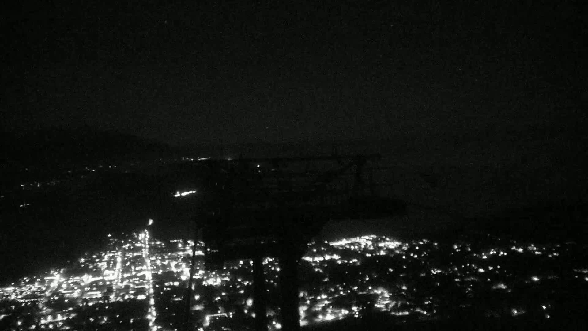 A nighttime view from an elevated position shows a city illuminated below, with a dark structure in the foreground.