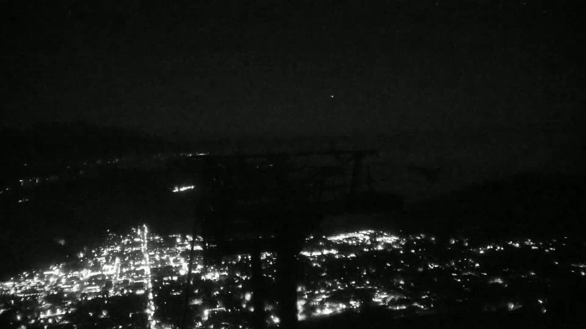 A nighttime, aerial view shows a sprawling city illuminated by countless small lights under a dark, clear sky.