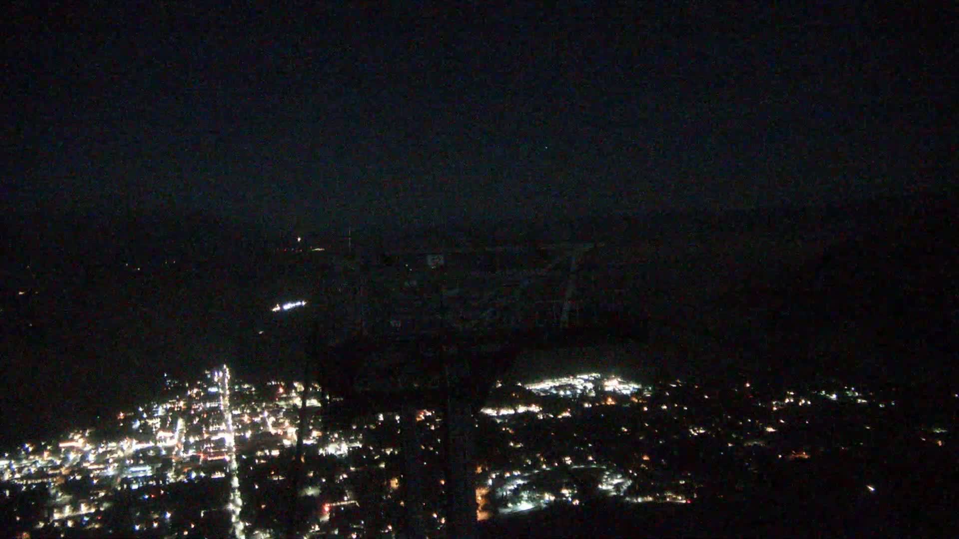 A nighttime, high-angle view shows a sprawling city illuminated by numerous lights under a dark, clear sky.
