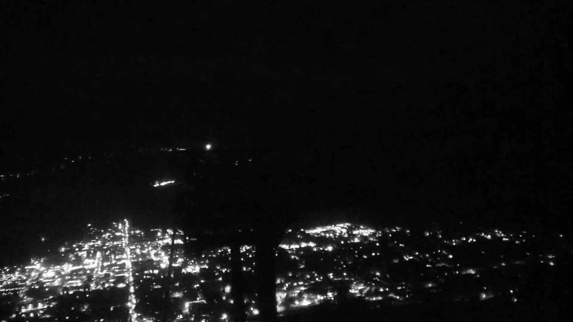 A nighttime view from a high vantage point shows a sprawling city illuminated by countless lights.