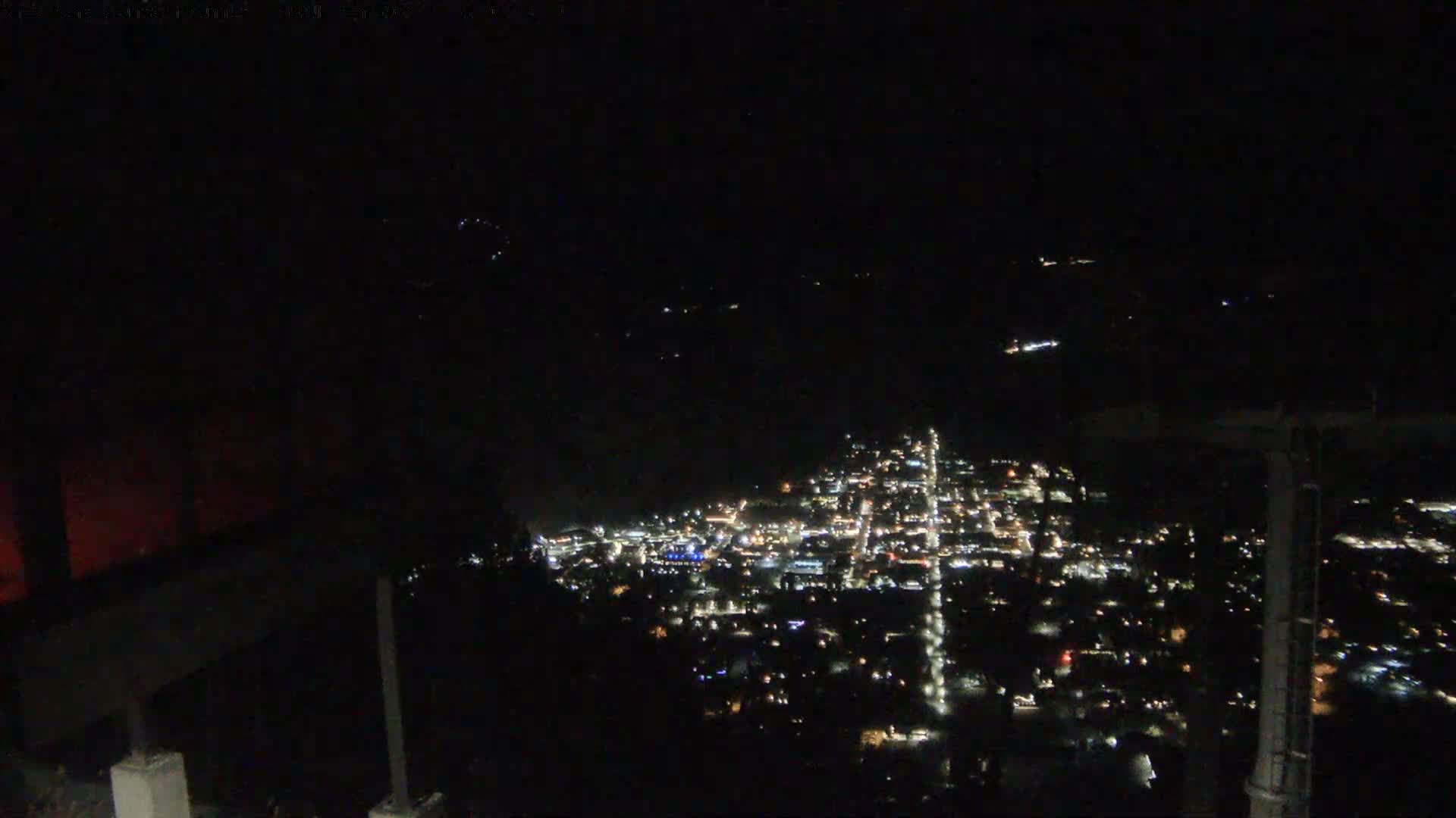 A clear night view captures a sprawling city sparkling with lights from an elevated perspective, set against a dark landscape and sky.