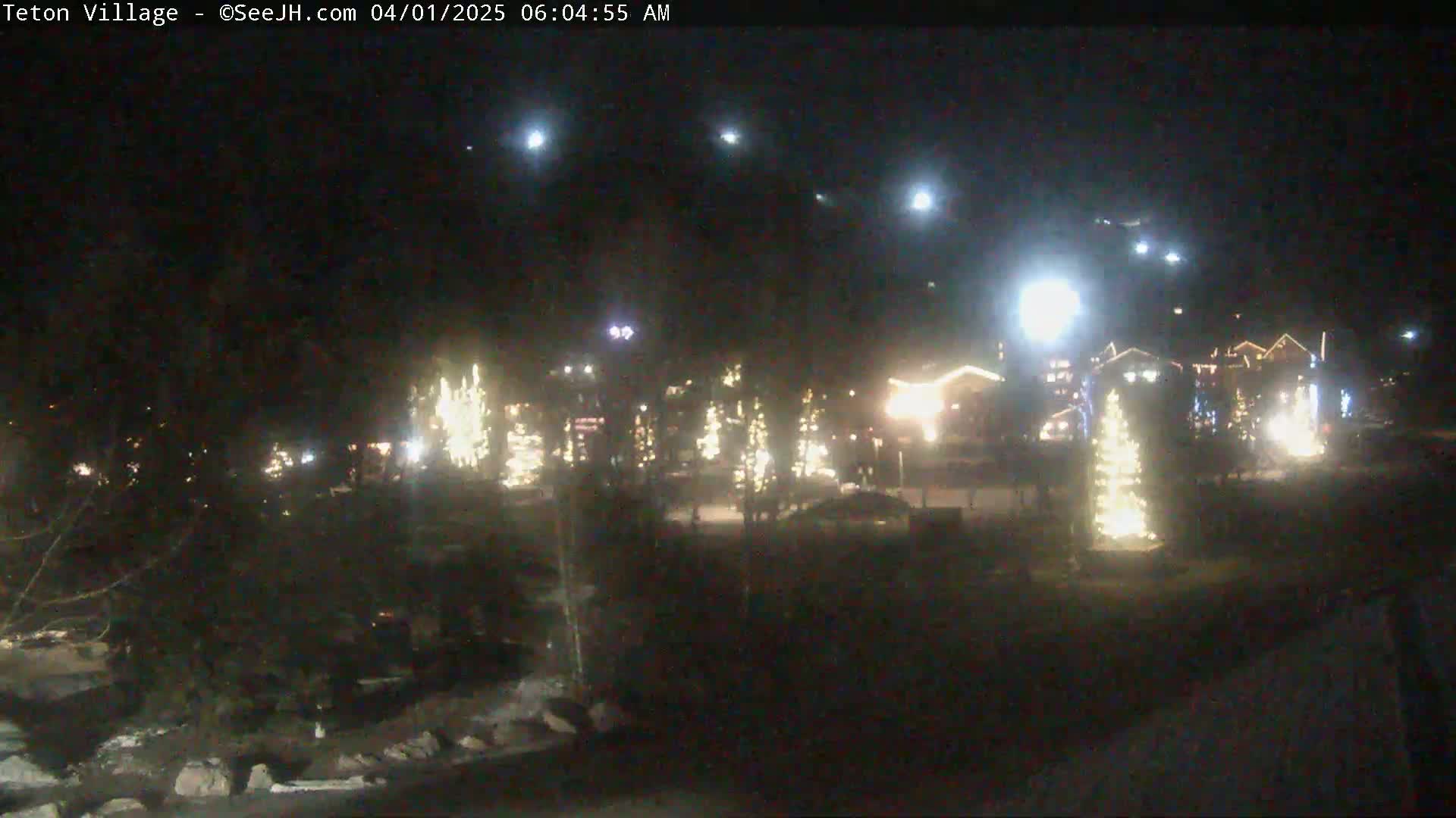 A nighttime view of a village illuminated with lights, under a clear sky with several bright stars visible.
