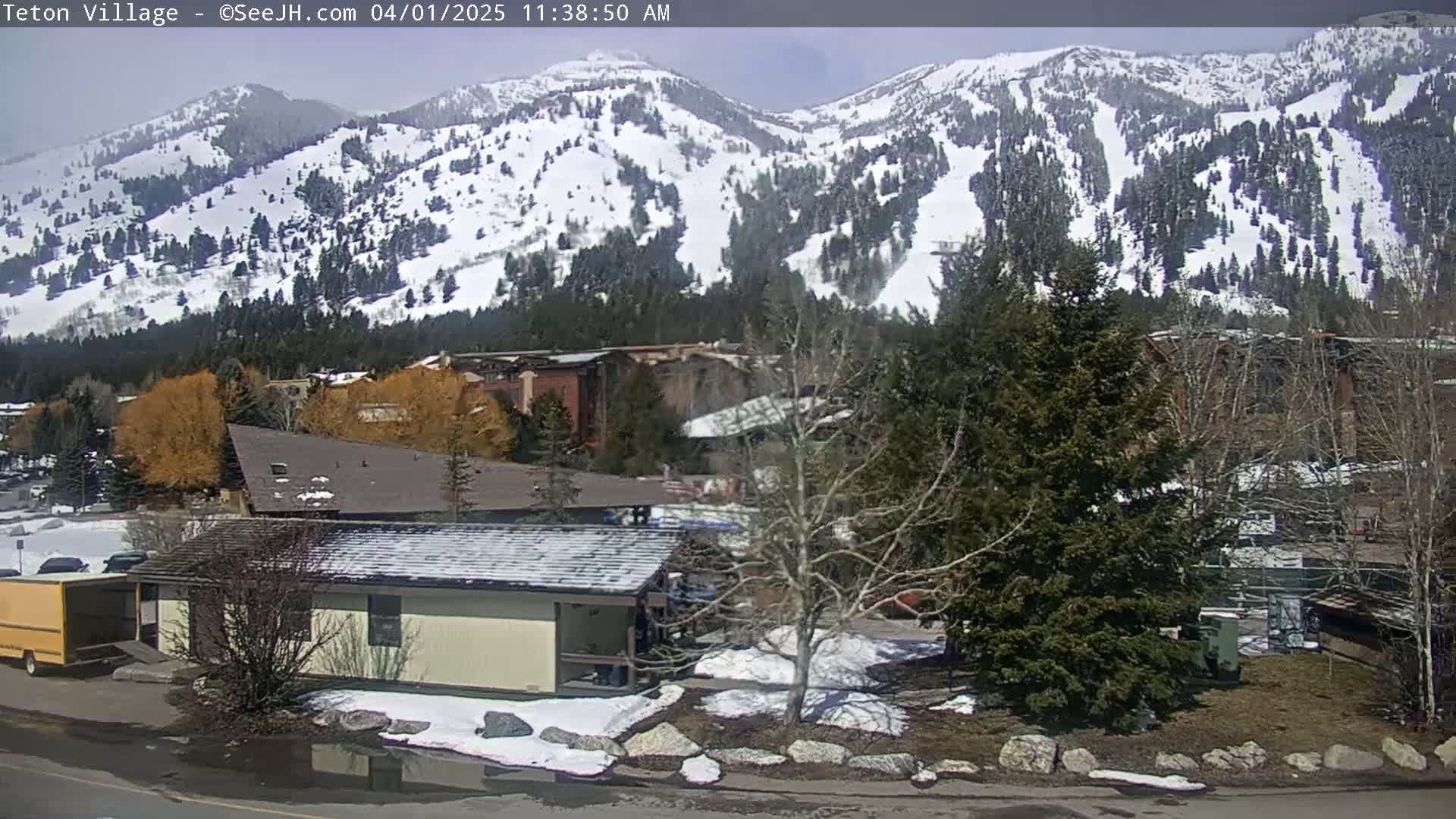 A snow-covered mountain range is visible in the background, with a small town situated in the foreground, under a partly sunny sky.
