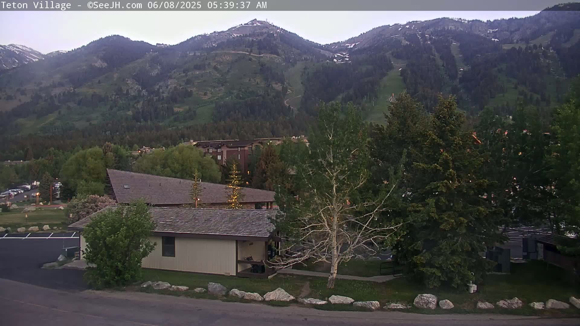 A low-light view shows a small building and surrounding landscaping in front of a mountain range under a mostly clear sky.