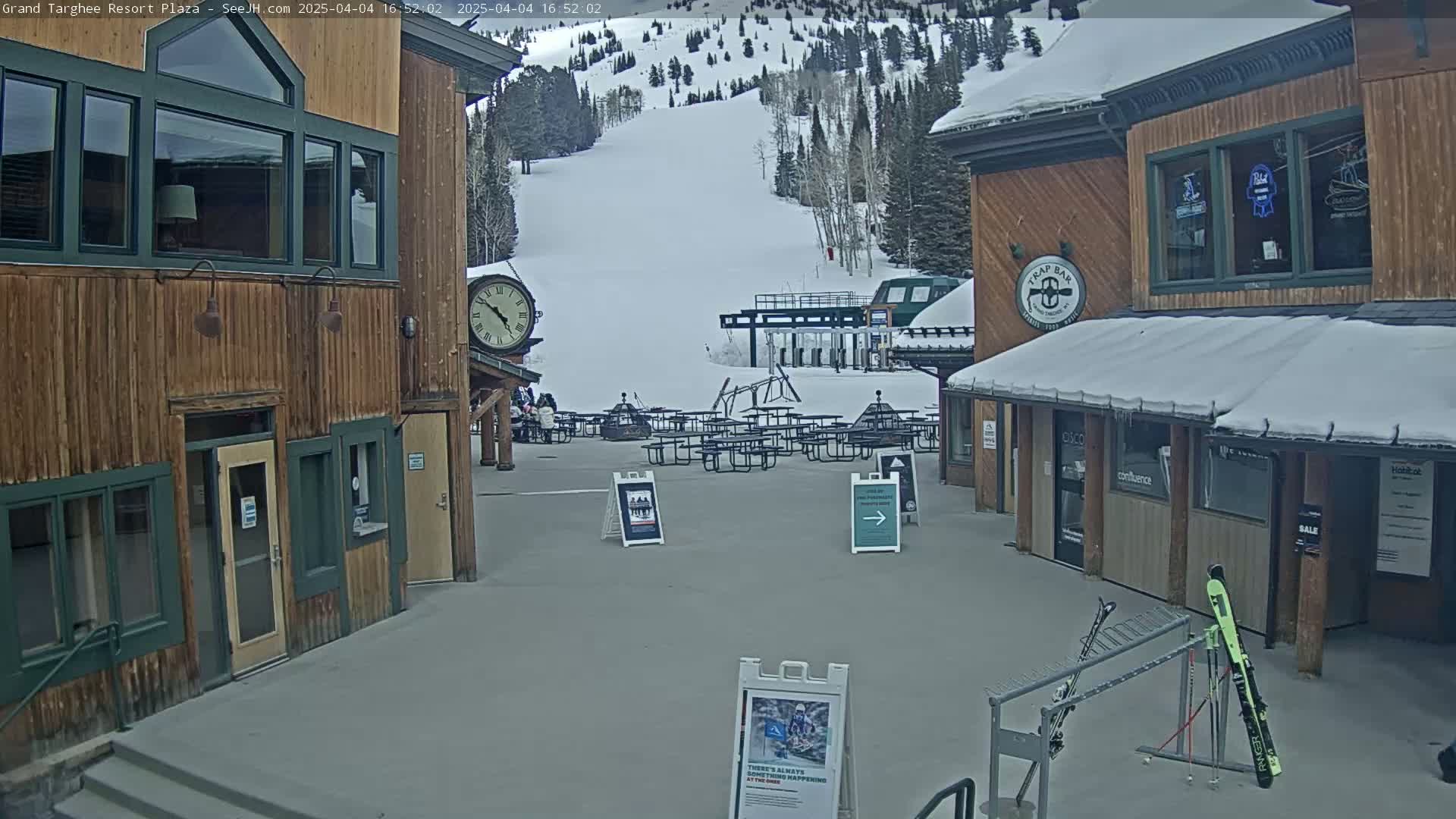 A plaza with wooden buildings, outdoor seating, and a ski lift in the background on a cloudy day with snow on the ground and buildings.