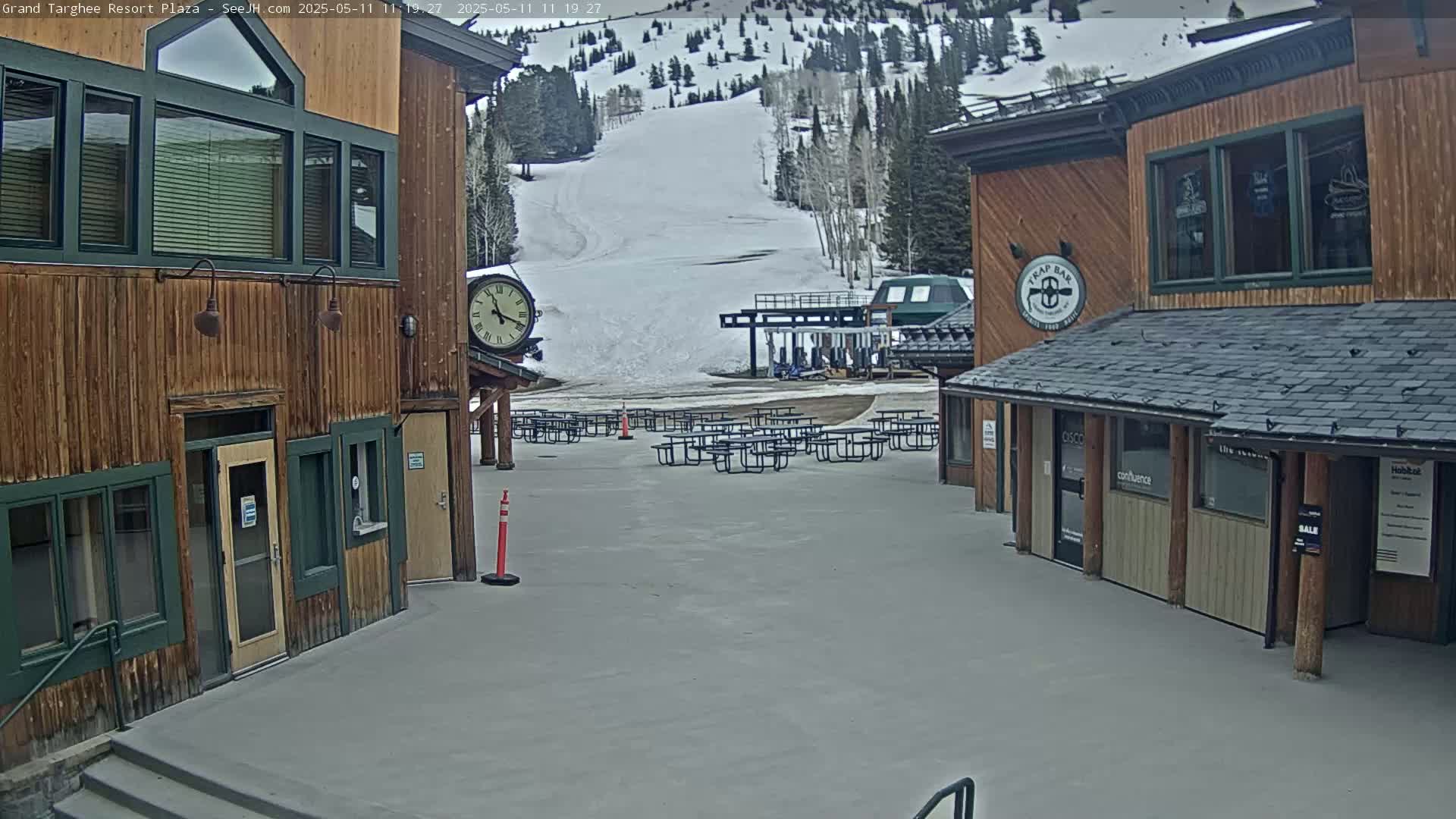 A plaza with wooden buildings, several picnic tables, and a ski lift in the background on an overcast day.