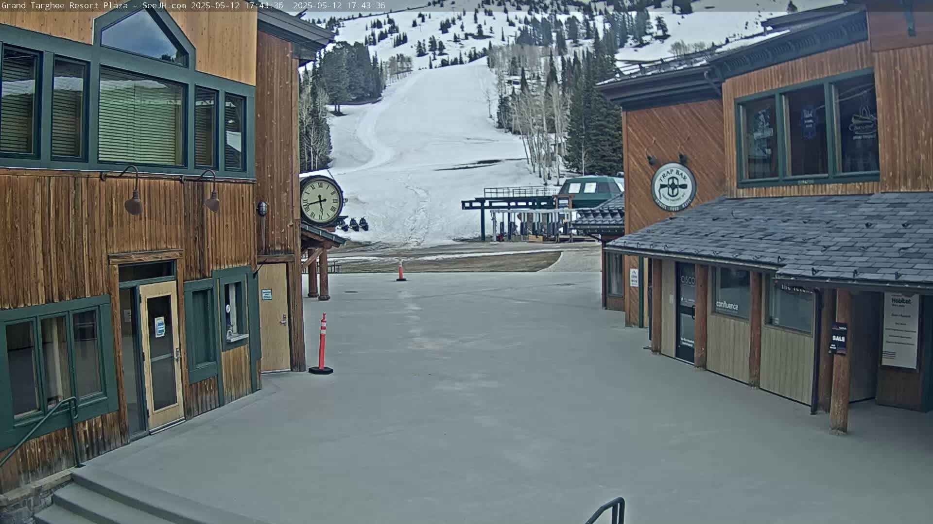 A plaza with two wooden buildings and a ski lift visible in the background on a partly cloudy day.