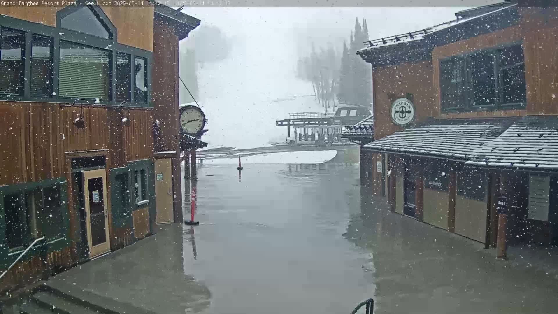 Snow falls on a plaza between two wooden buildings, with the plaza appearing flooded.