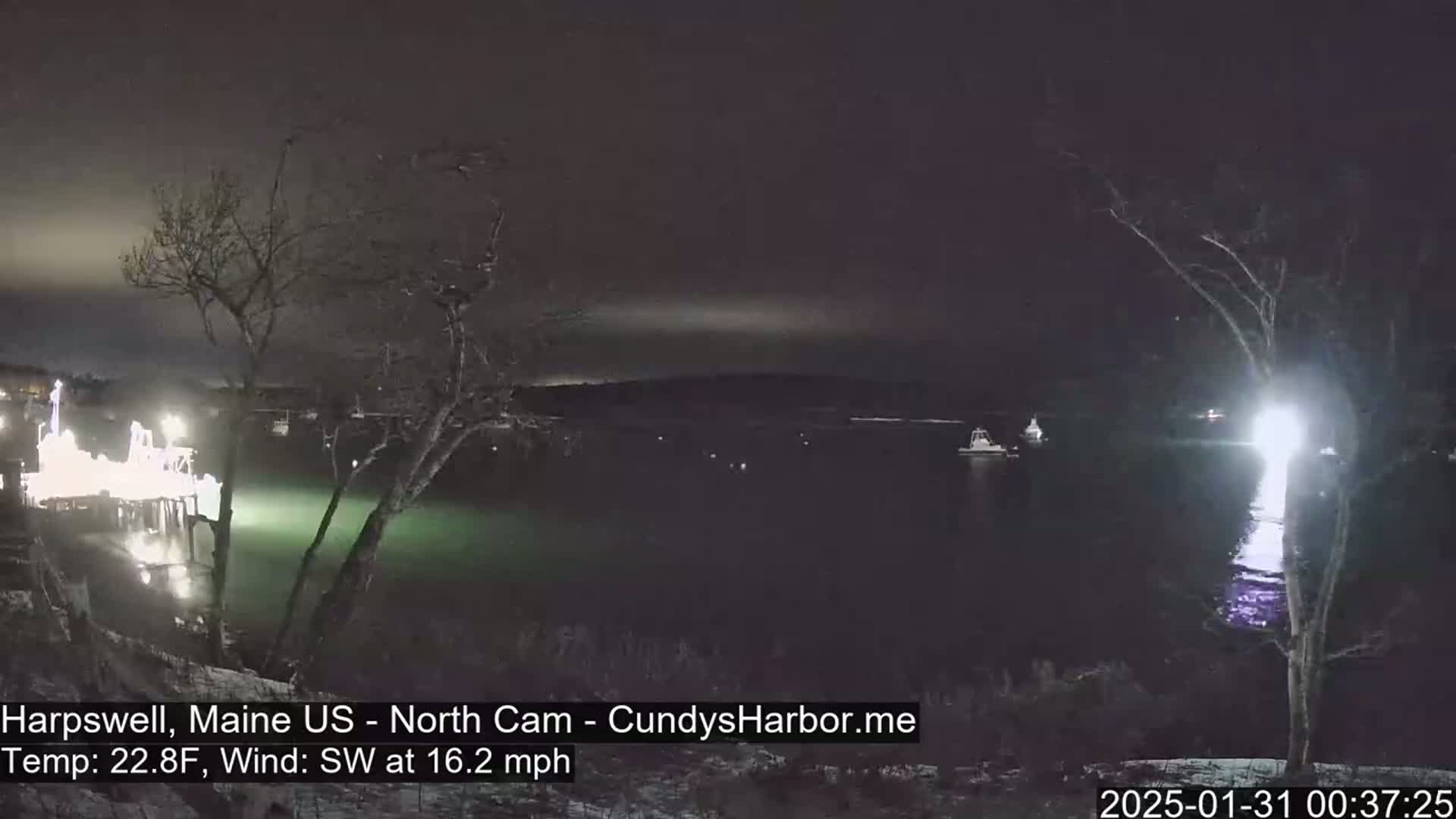 A nighttime view of a harbor with a brightly lit pier and several boats, under a dark sky with a southwest wind at 16.2 mph.