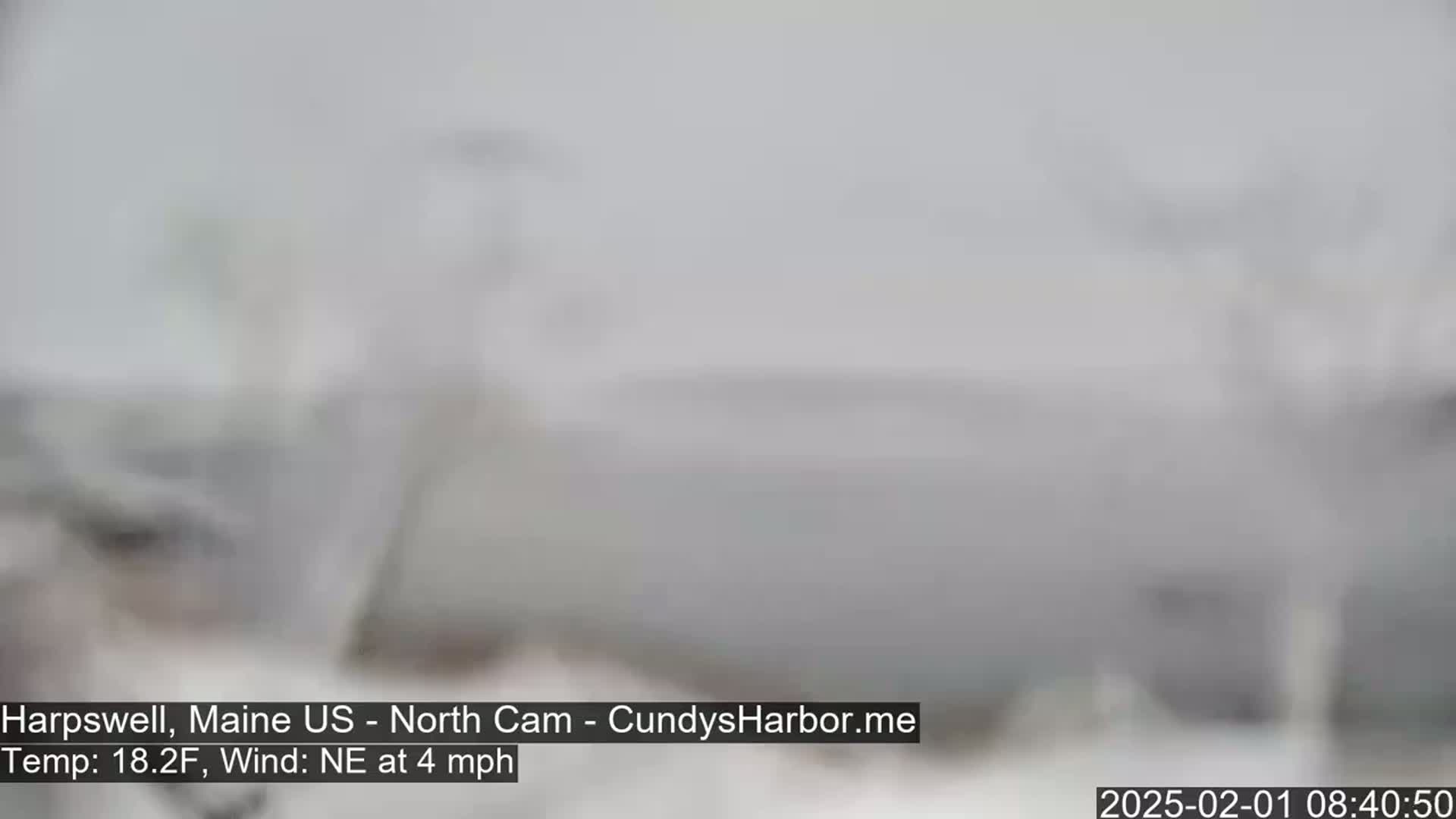 A blurry, snow-filled outdoor scene shows a mostly white landscape with a northeast wind at 4 mph and a temperature of 18.2 degrees Fahrenheit.