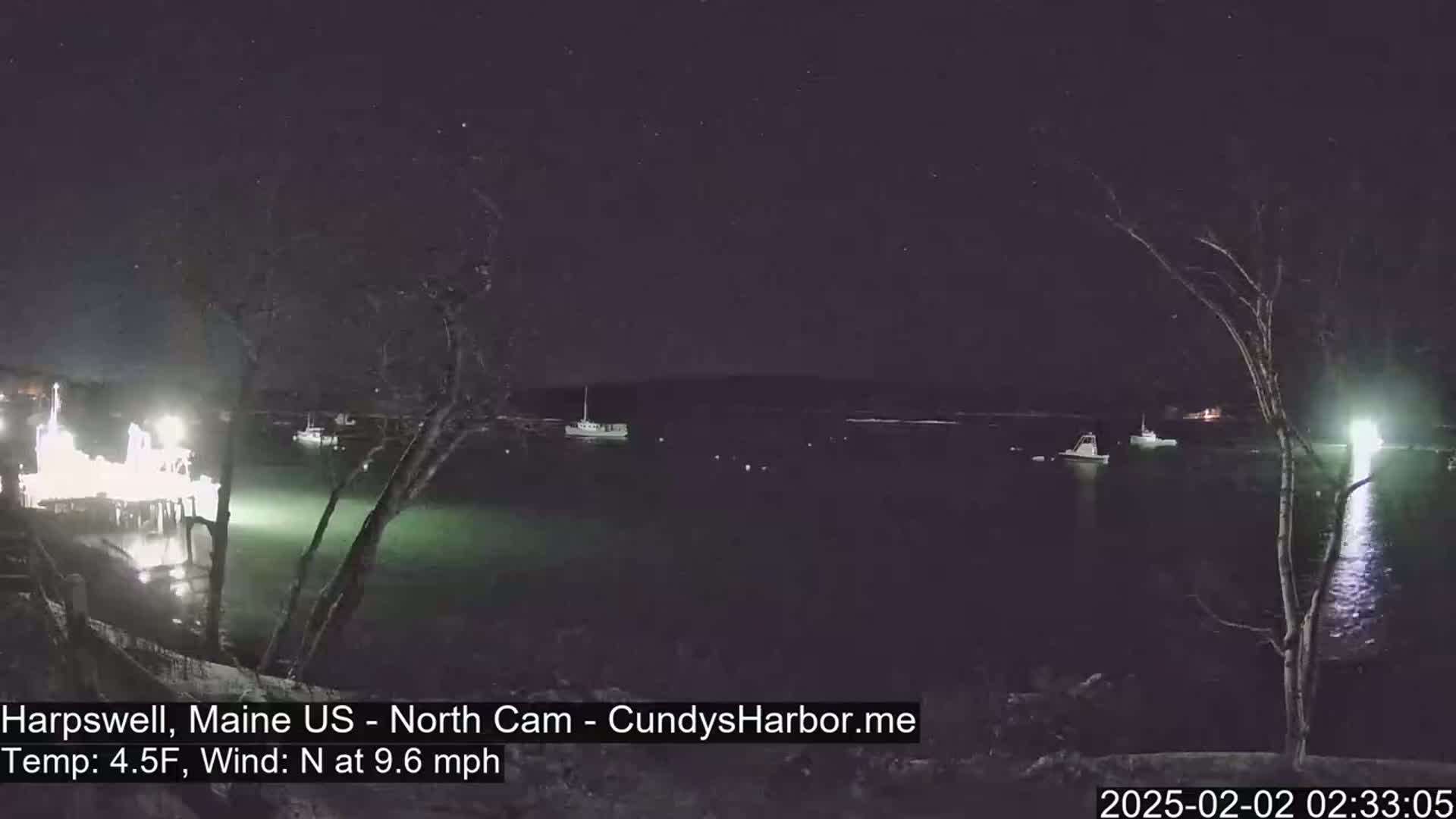 A nighttime view of a harbor with several boats, under a starry sky and a north wind of 9.6 mph at 4.5°F.