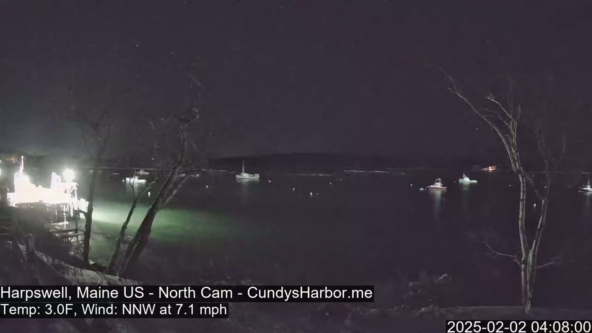 A nighttime view of a harbor with several boats, under a clear, starry sky and a 3°F temperature with a 7.1 mph north-northwest wind.