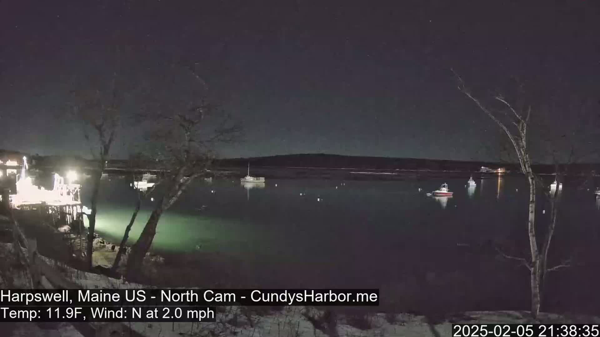 A nighttime view of a calm harbor with several boats, under a dark, starry sky, and a light north wind.