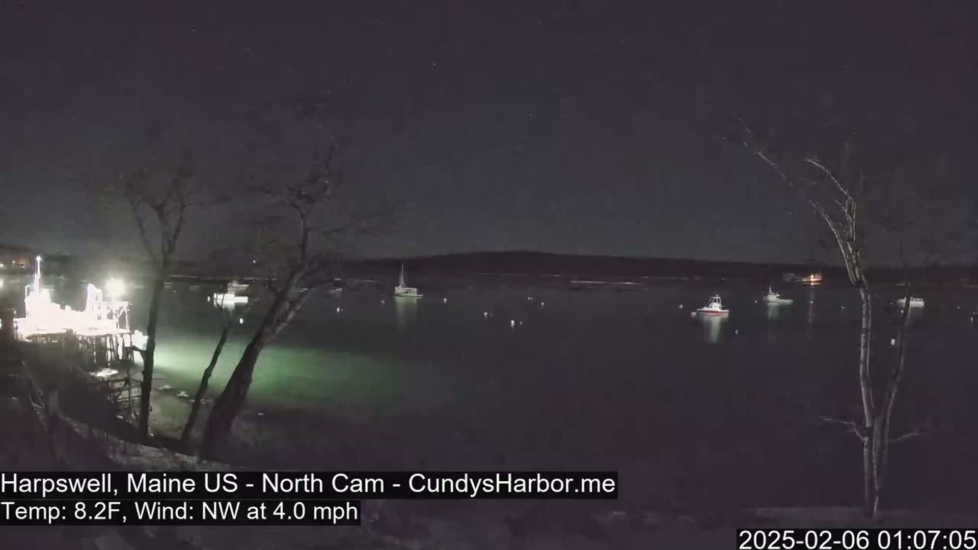 Several boats are moored in a dark, calm harbor at night under a starry sky, with a gentle northwest wind.