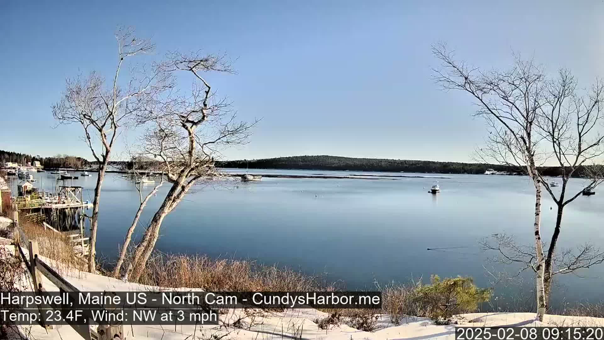 A calm, clear, and cold day with a light northwest wind shows a harbor view with several boats, bare trees, and a snow-dusted shoreline.
