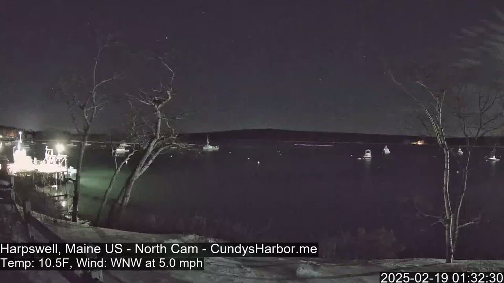 A nighttime view of a harbor with several boats at rest, under a clear, starry sky, and a temperature of 10.5°F with a west-northwest wind at 5.0 mph.