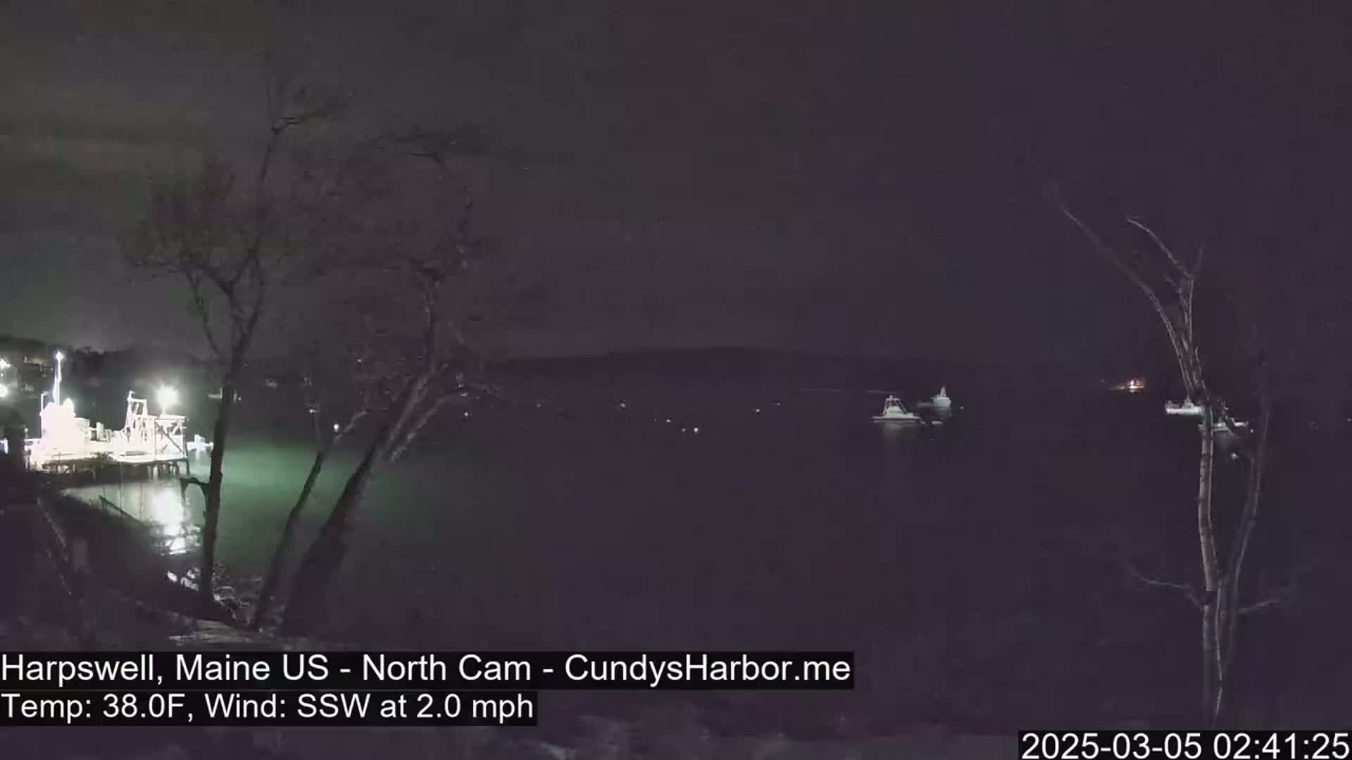 A nighttime view of a dark body of water with several boats and a dock, under a clear sky and a light south-southwesterly wind.